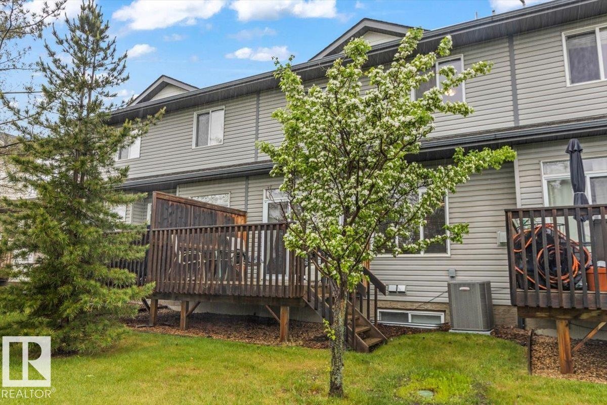 Rear exterior featuring light gray siding, multiple windows, and a dark wood-finish deck with privacy screening - 229 41 Summerwood Boulevard, Sherwood Park, AB - Outdoor With Deck Patio Veranda With Exterior