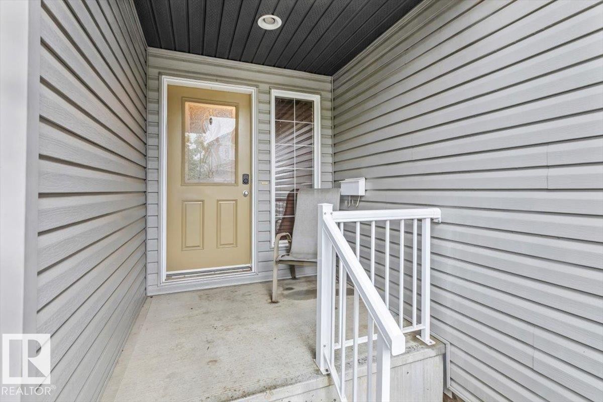 Covered entryway featuring light gray horizontal siding, a beige paneled entry door with frosted glass, and a side window with horizontal blinds - 229 41 Summerwood Boulevard, Sherwood Park, AB - Outdoor With Exterior