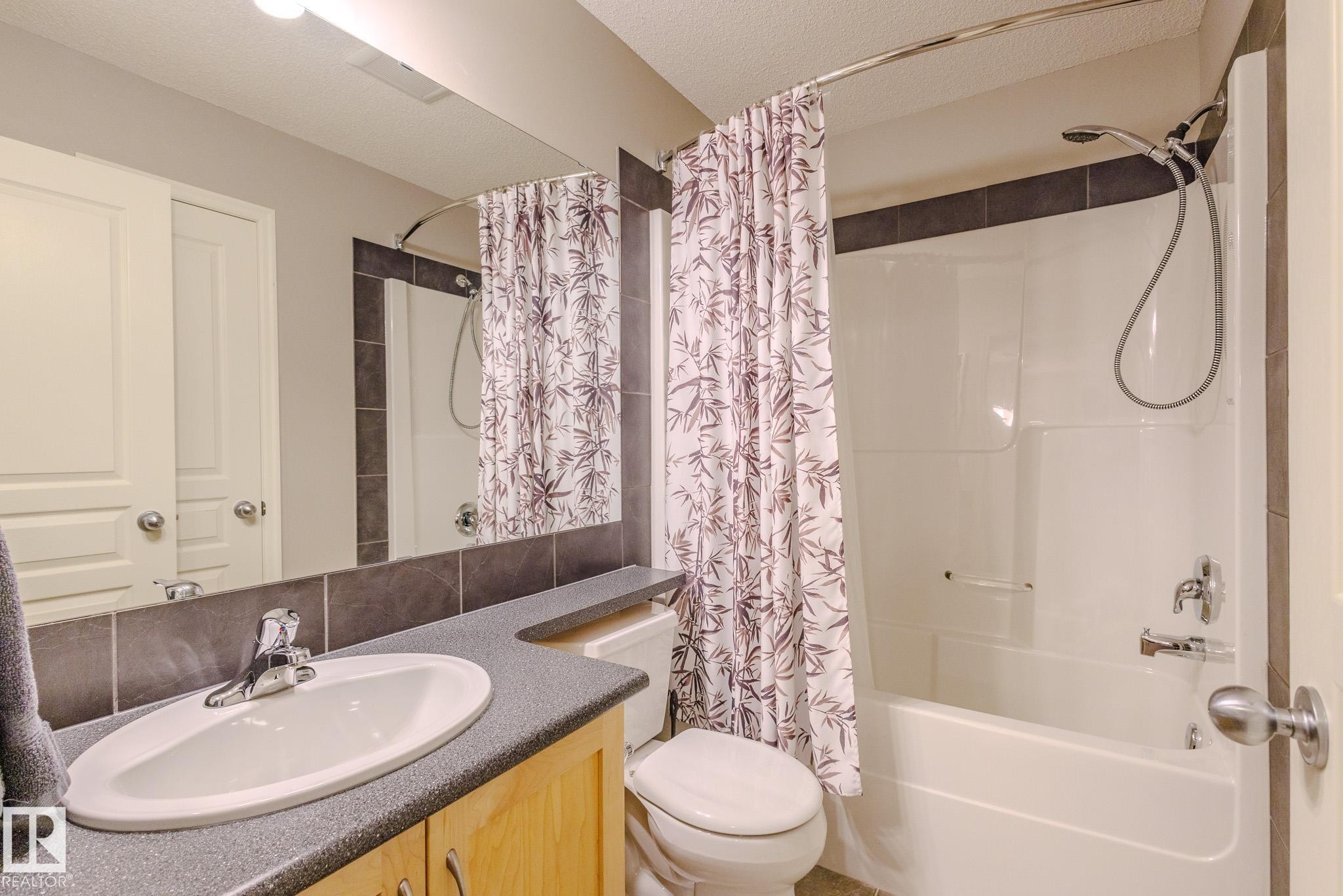 Bathroom featuring a built-in vanity with a dark speckled countertop, an integrated sink with a chrome faucet, and a large mirror extending to the ceiling - 7207 14A Avenue, Edmonton, AB - Indoor Photo Showing Bathroom