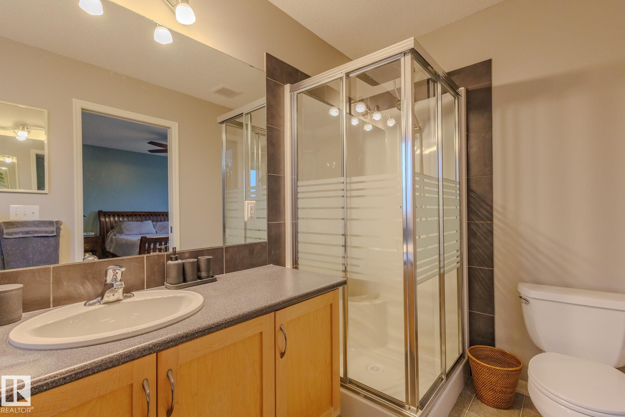 Glass-enclosed shower with frosted privacy bands, complemented by a single-sink vanity with light wood cabinetry and a dark countertop - 7207 14A Avenue, Edmonton, AB - Indoor Photo Showing Bathroom