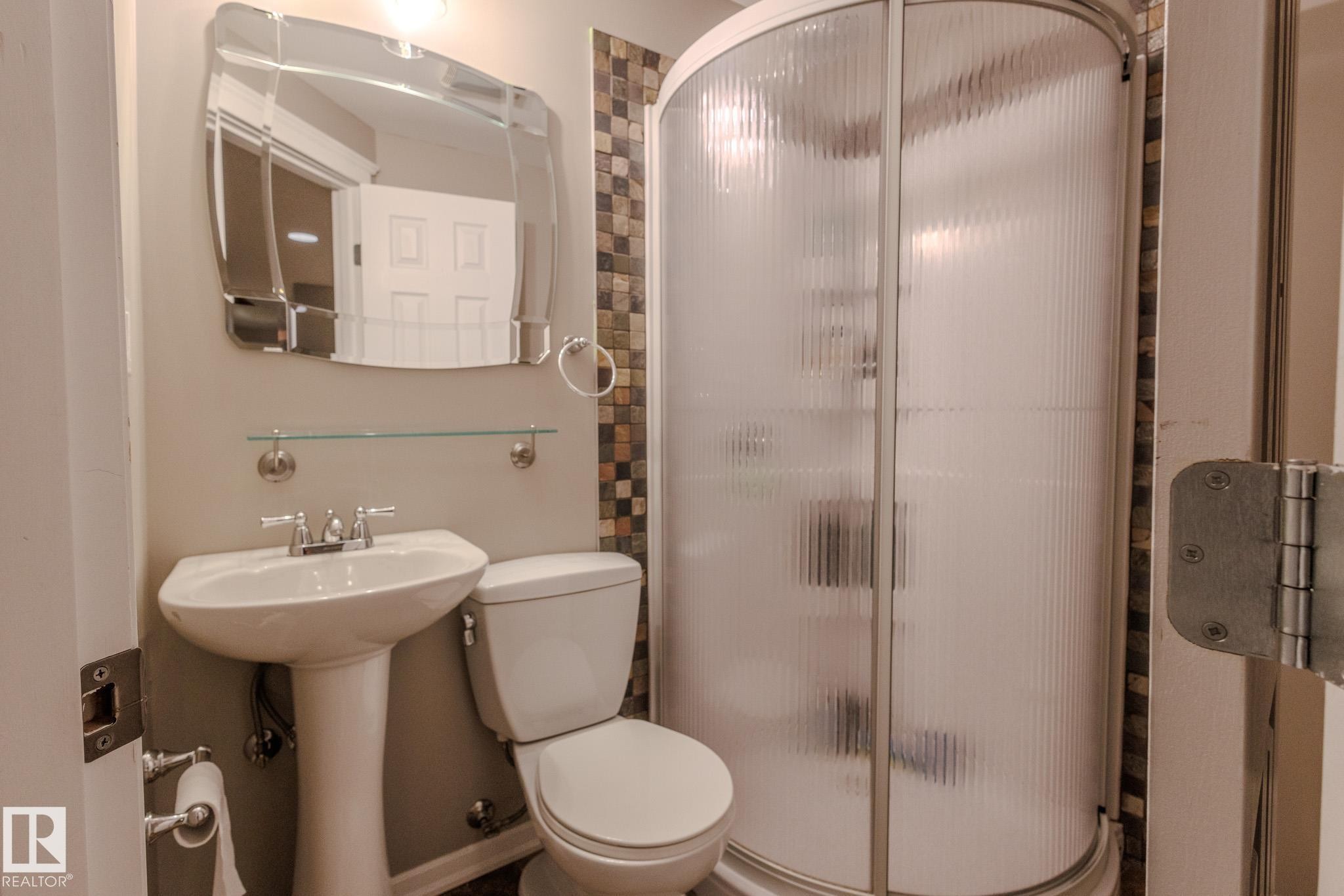 Pedestal sink with chrome faucet, complemented by a decorative mirror and glass shelf - 7207 14A Avenue, Edmonton, AB - Indoor Photo Showing Bathroom