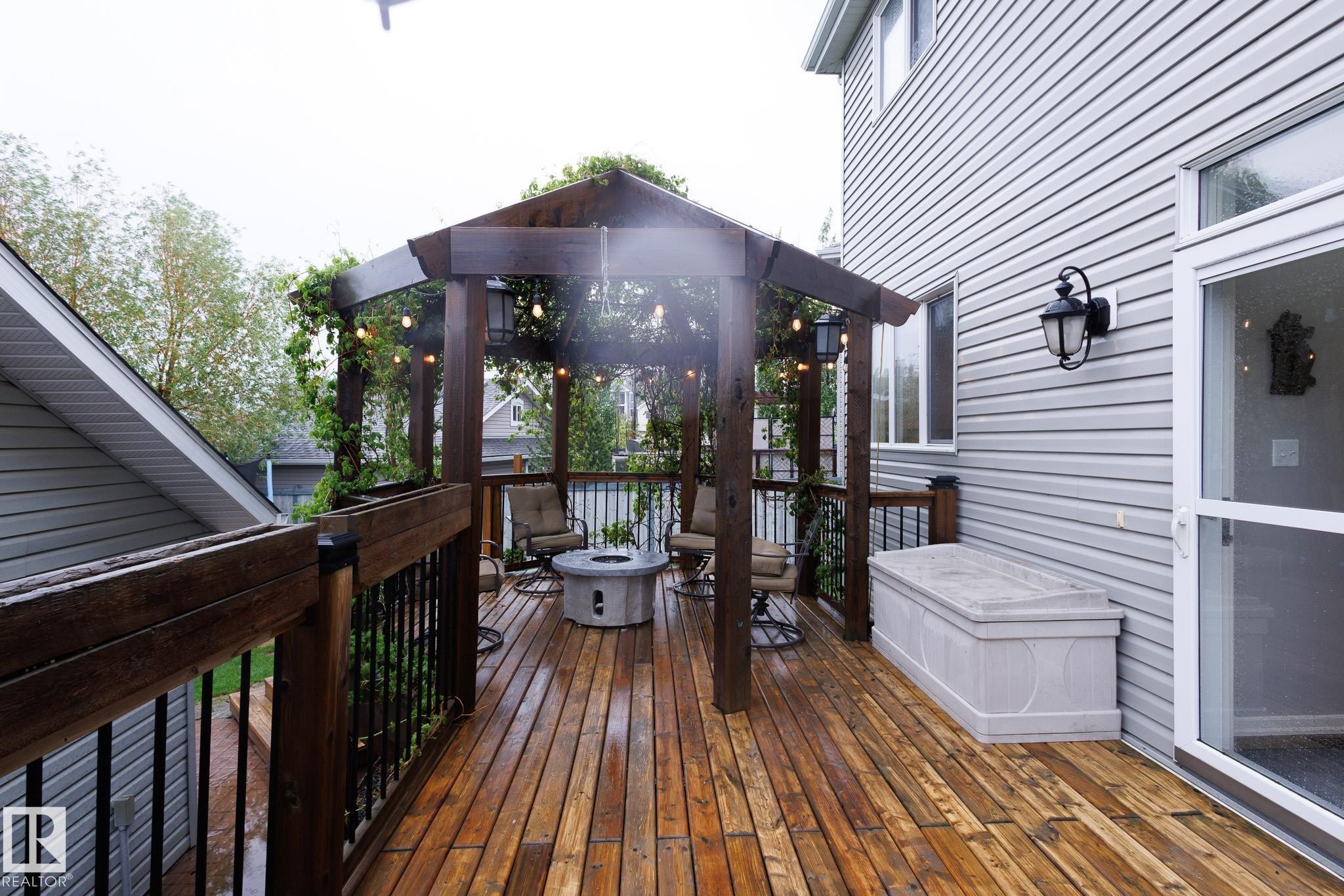 Expansive wood-finish deck featuring a pergola with string lighting, black metal railings, and a built-in hot tub - 7207 14A Avenue, Edmonton, AB - Outdoor With Exterior