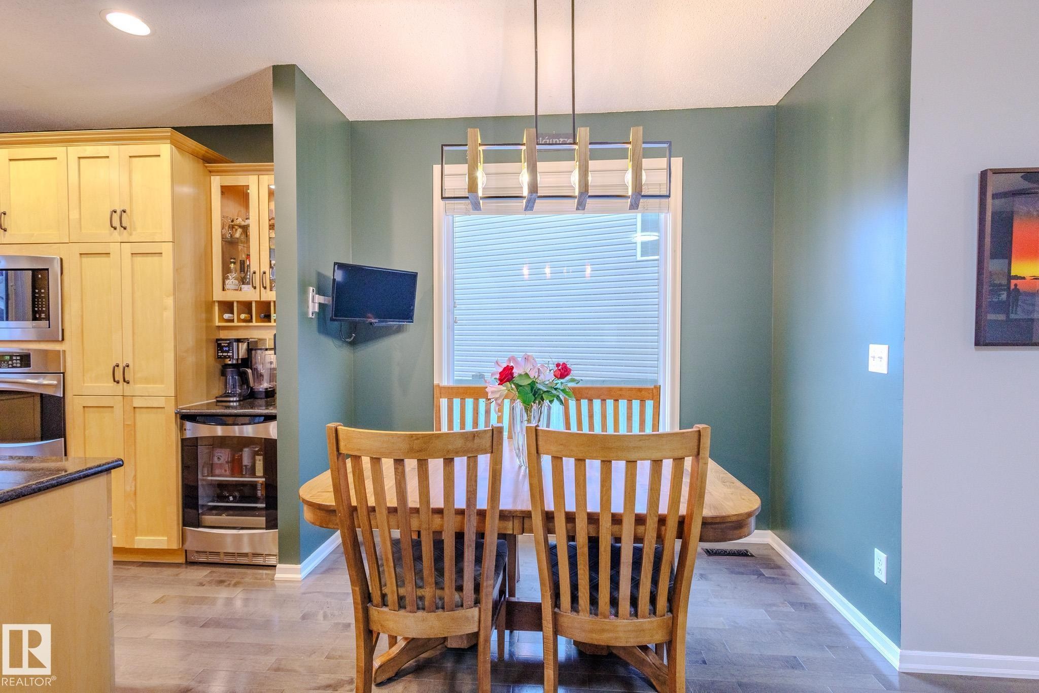 Dining area featuring a contemporary linear chandelier, large window with blinds, and wood-finish flooring - 7207 14A Avenue, Edmonton, AB - Indoor Photo Showing Dining Room