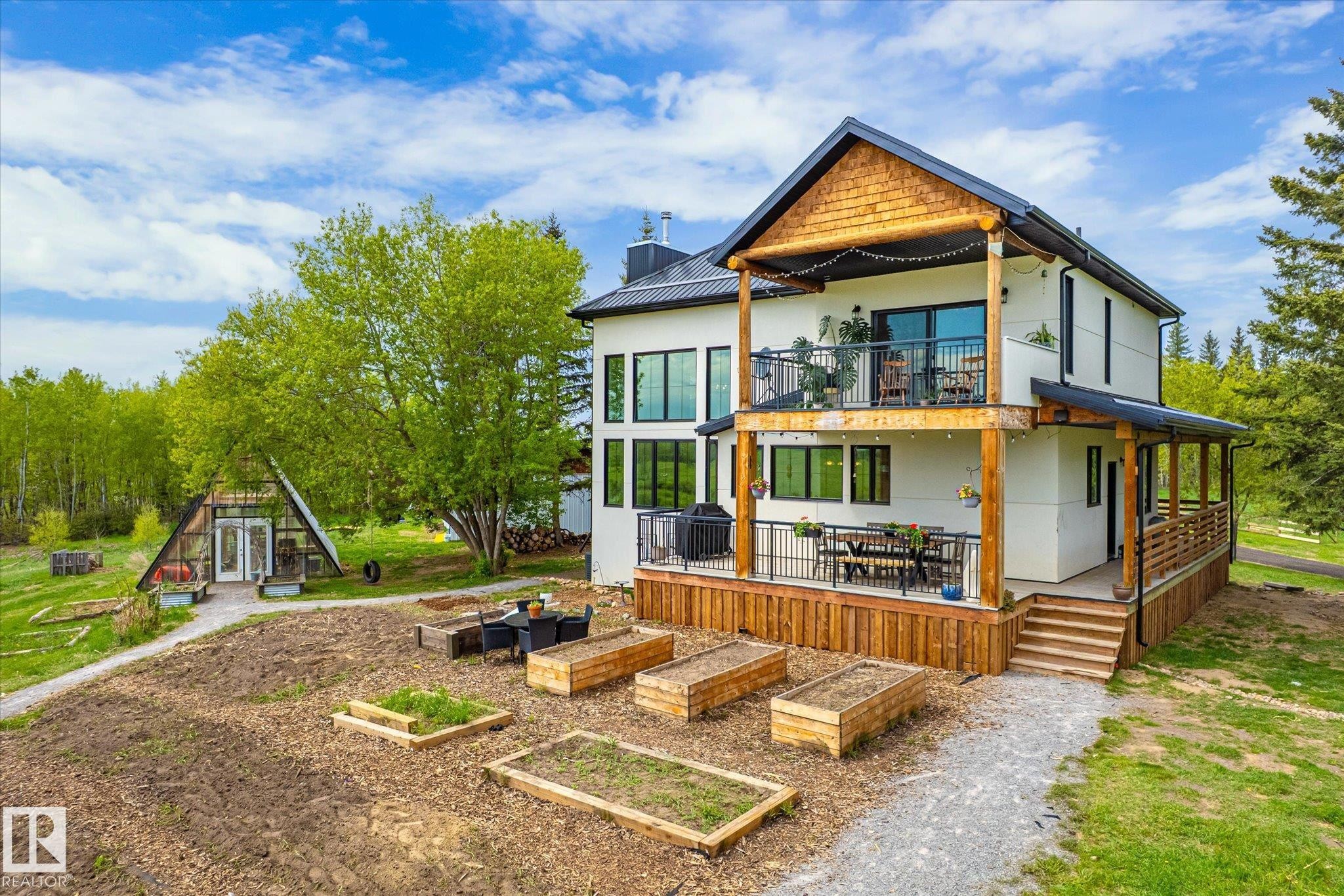 Two-story residence featuring a ground-level deck with wooden railing and a second-story balcony with metal railing - 59102 Rge Road 234, Rural Westlock County, AB