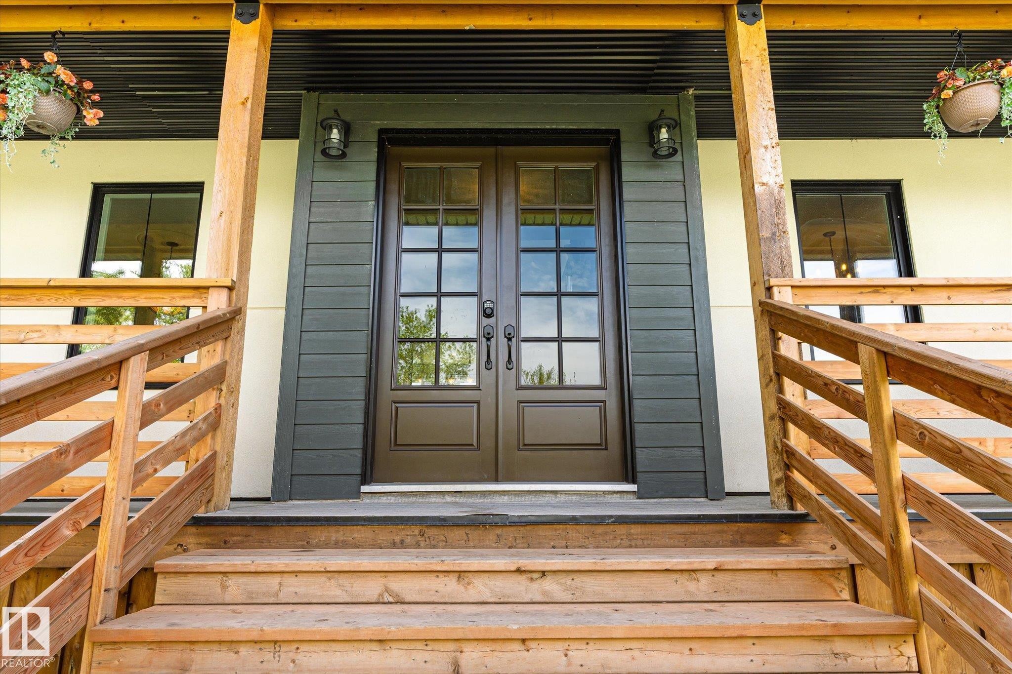 Entryway featuring double doors with glass panes, wood steps, coordinating wood railings, black exterior sconces, and dark horizontal siding accents - 59102 Rge Road 234, Rural Westlock County, AB