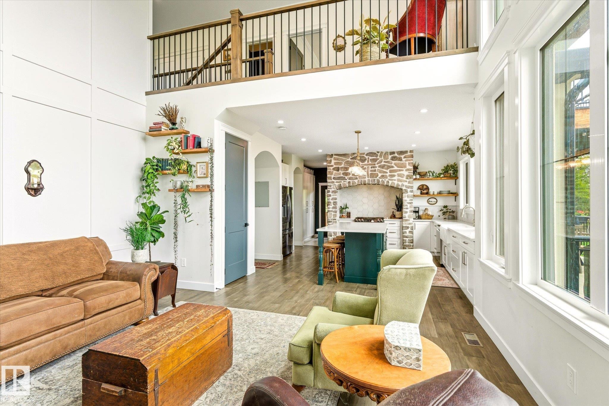 Two-story living area with wood-finish flooring, a stone-accented kitchen, and an upper-level balcony with metal balusters - 59102 Rge Road 234, Rural Westlock County, AB