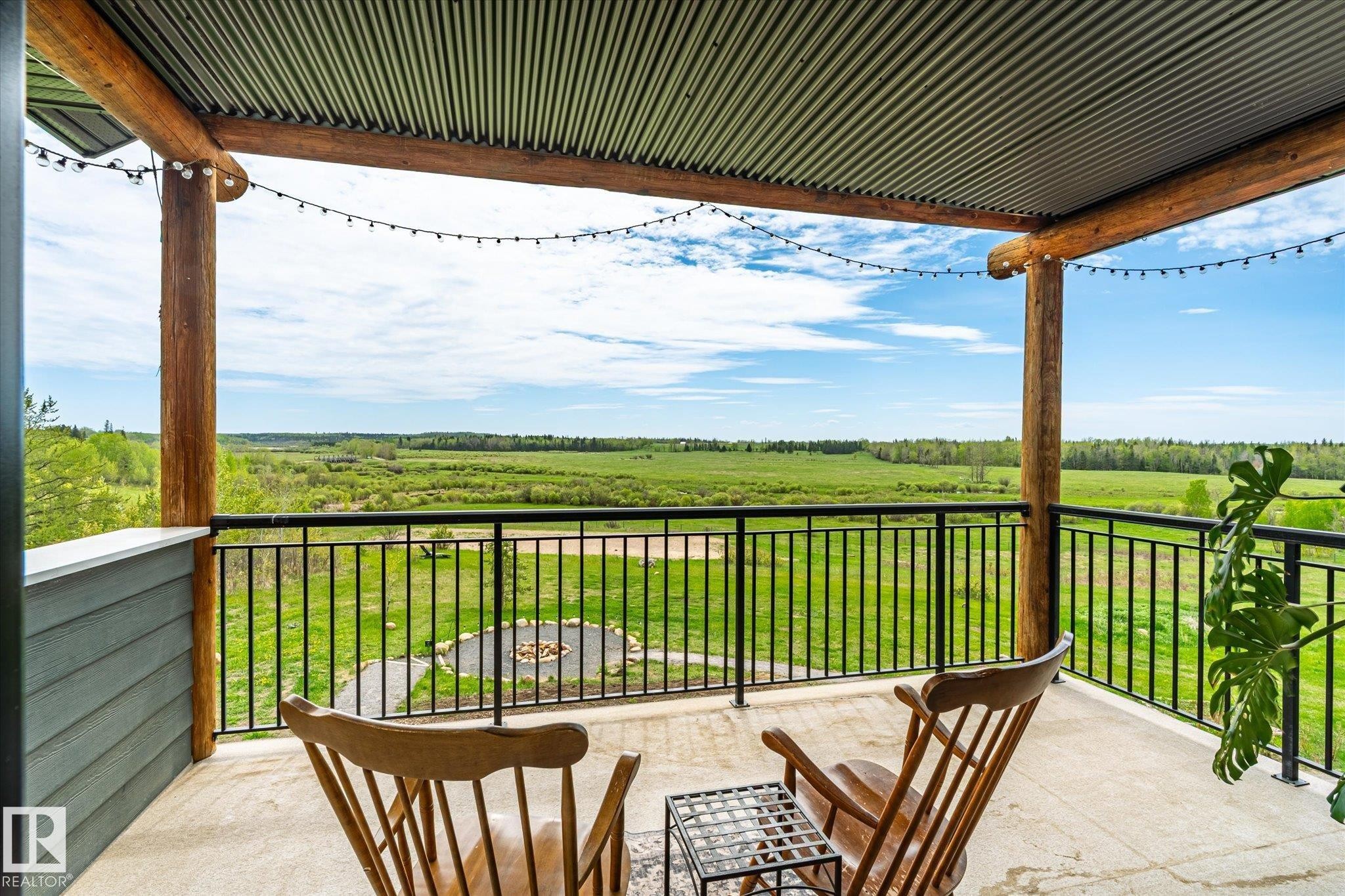 Covered outdoor deck with exposed log beams, corrugated metal ceiling, dark metal railing, and concrete flooring - 59102 Rge Road 234, Rural Westlock County, AB