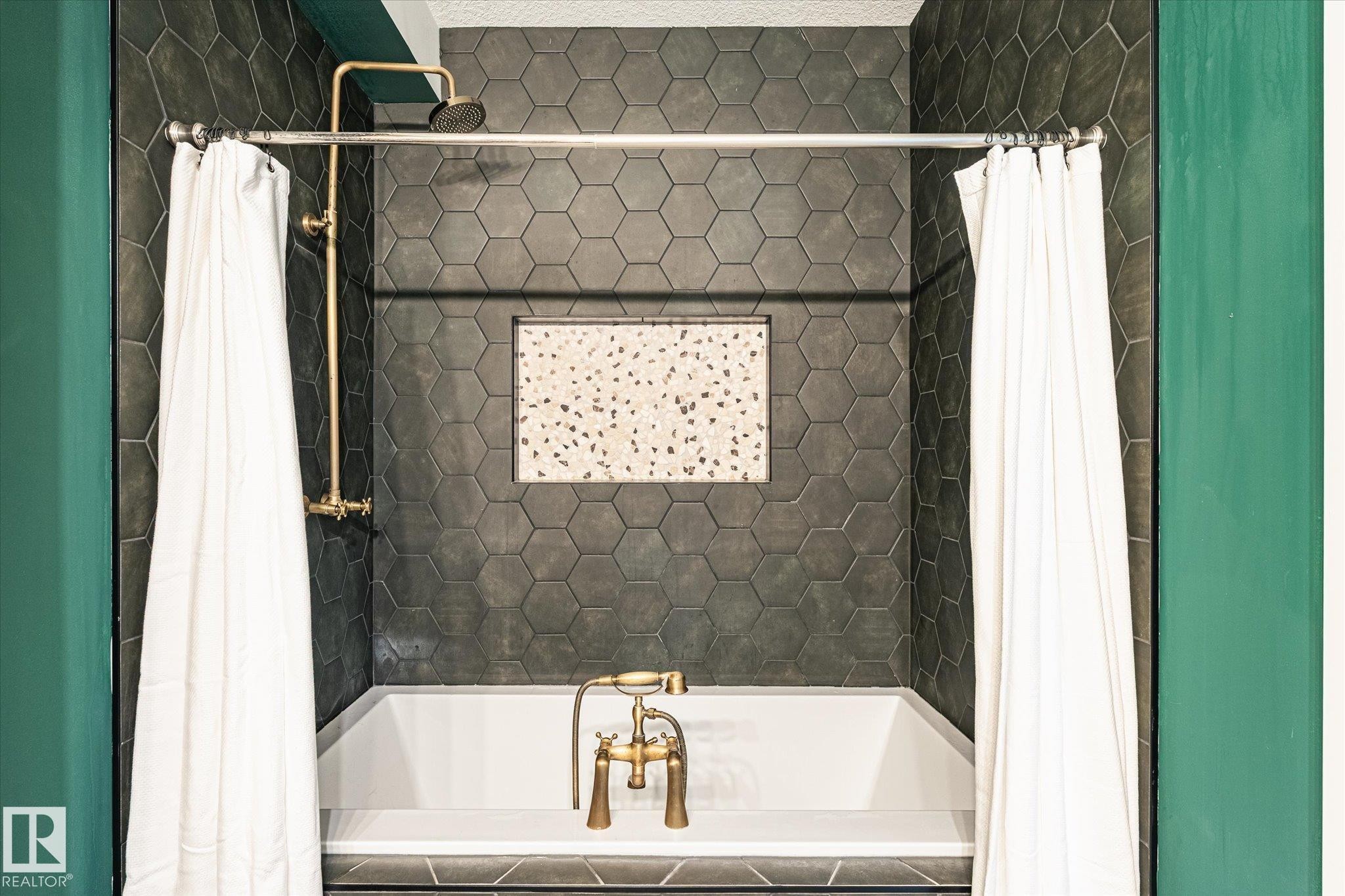 Bathtub with hexagonal dark tile surround, brass fixtures, and a recessed niche featuring speckled tile - 59102 Rge Road 234, Rural Westlock County, AB