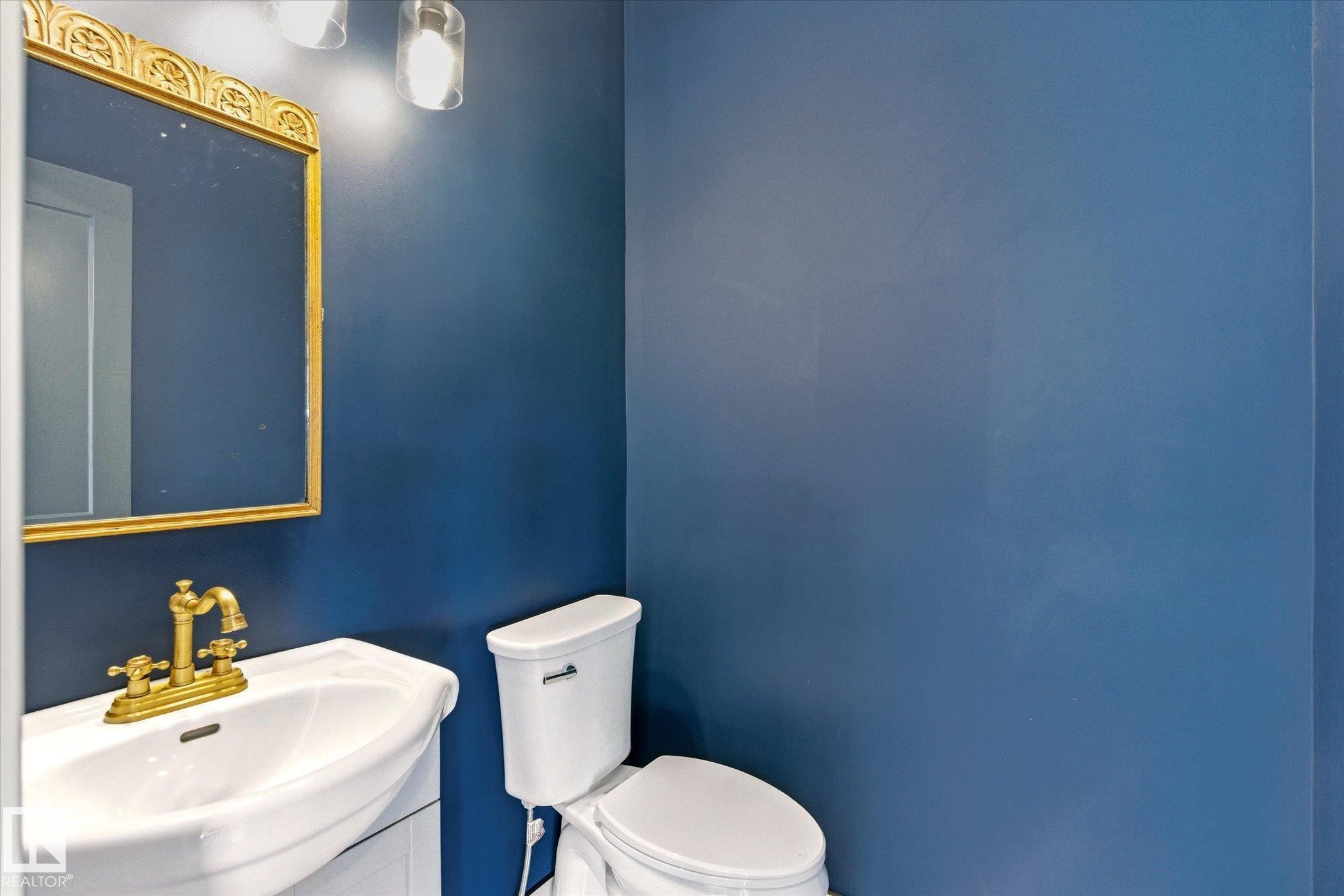 Powder room featuring a pedestal sink with brass-finish faucet, a white toilet, and a decorative gold-frame mirror - 59102 Rge Road 234, Rural Westlock County, AB