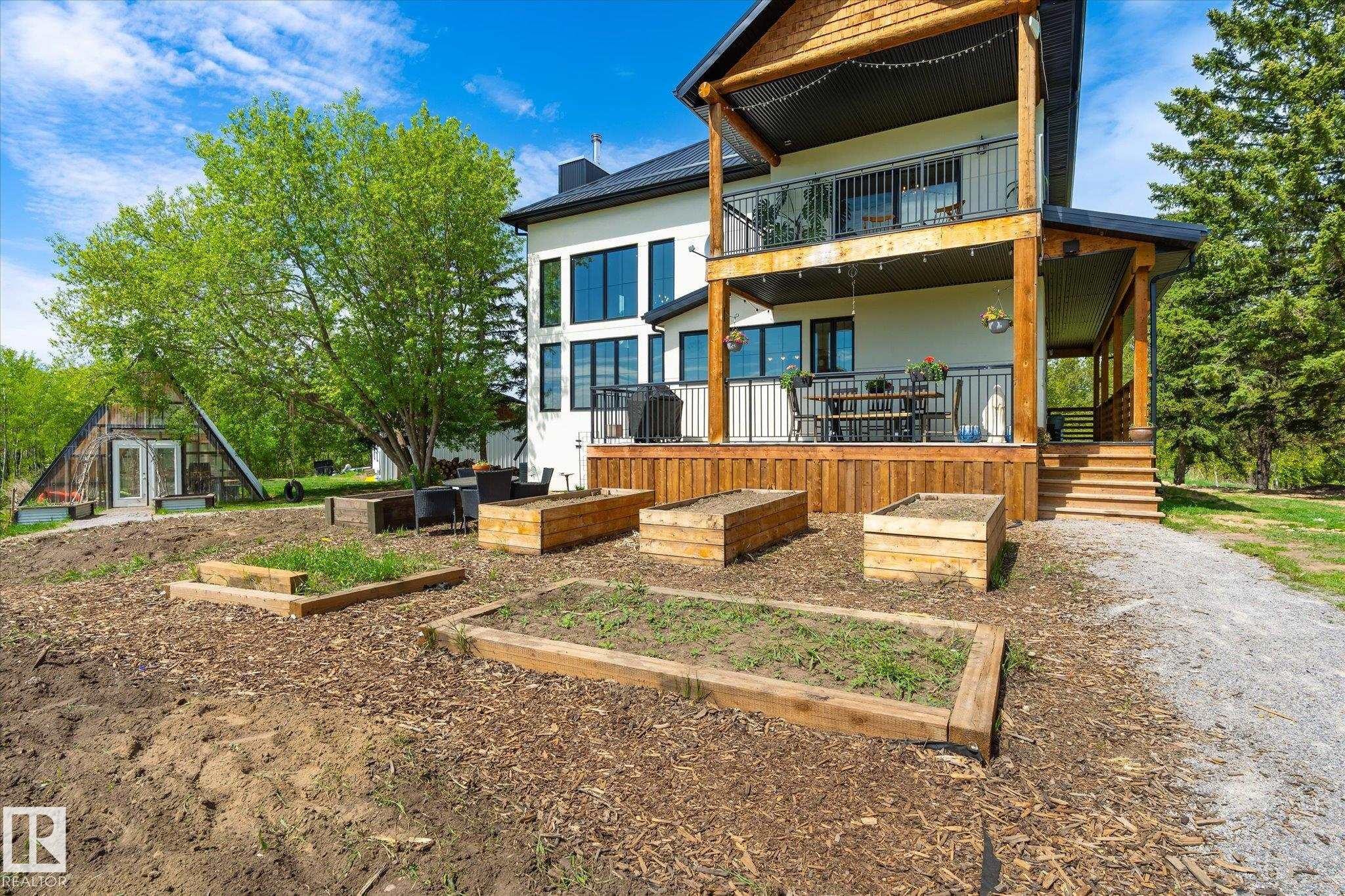 Rear exterior featuring a spacious wood deck, covered patio, second-story balcony, raised garden beds, and a distinctive A-frame structure - 59102 Rge Road 234, Rural Westlock County, AB