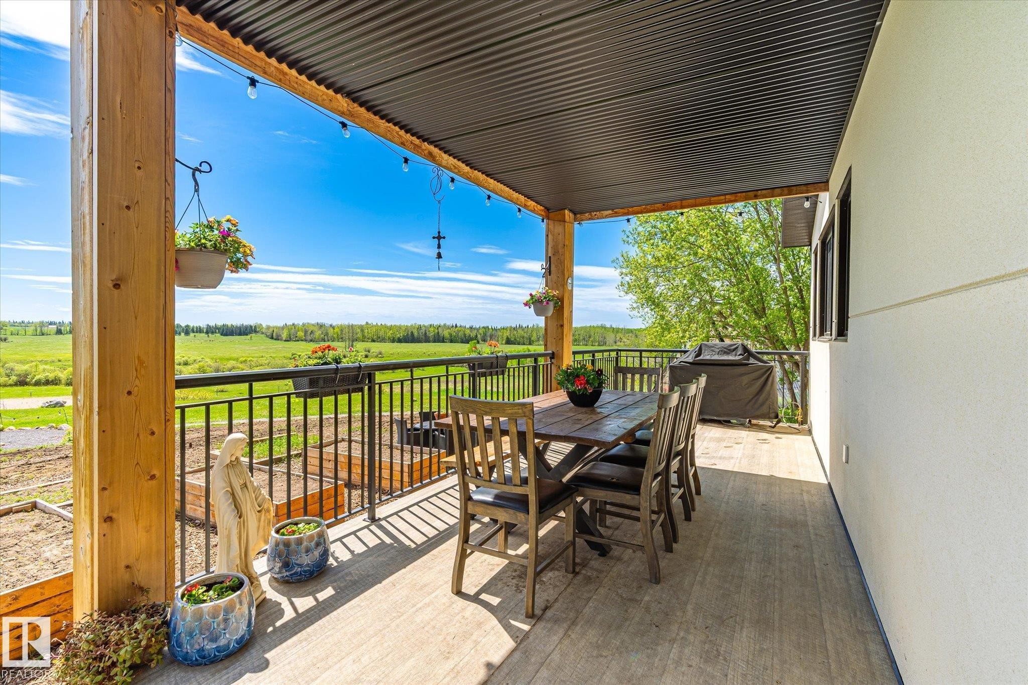 Covered outdoor deck featuring wood-finish flooring, a corrugated metal ceiling, and a black metal railing - 59102 Rge Road 234, Rural Westlock County, AB