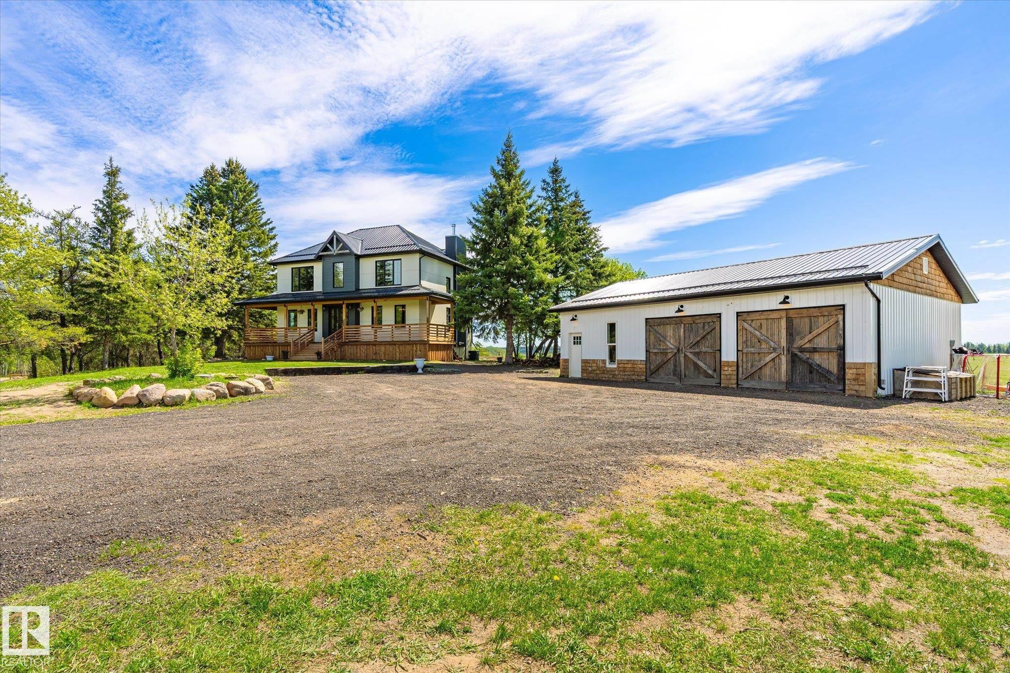 Two-story residence featuring a multi-gable roofline, covered porch, and a gravel driveway - 59102 Rge Road 234, Rural Westlock County, AB