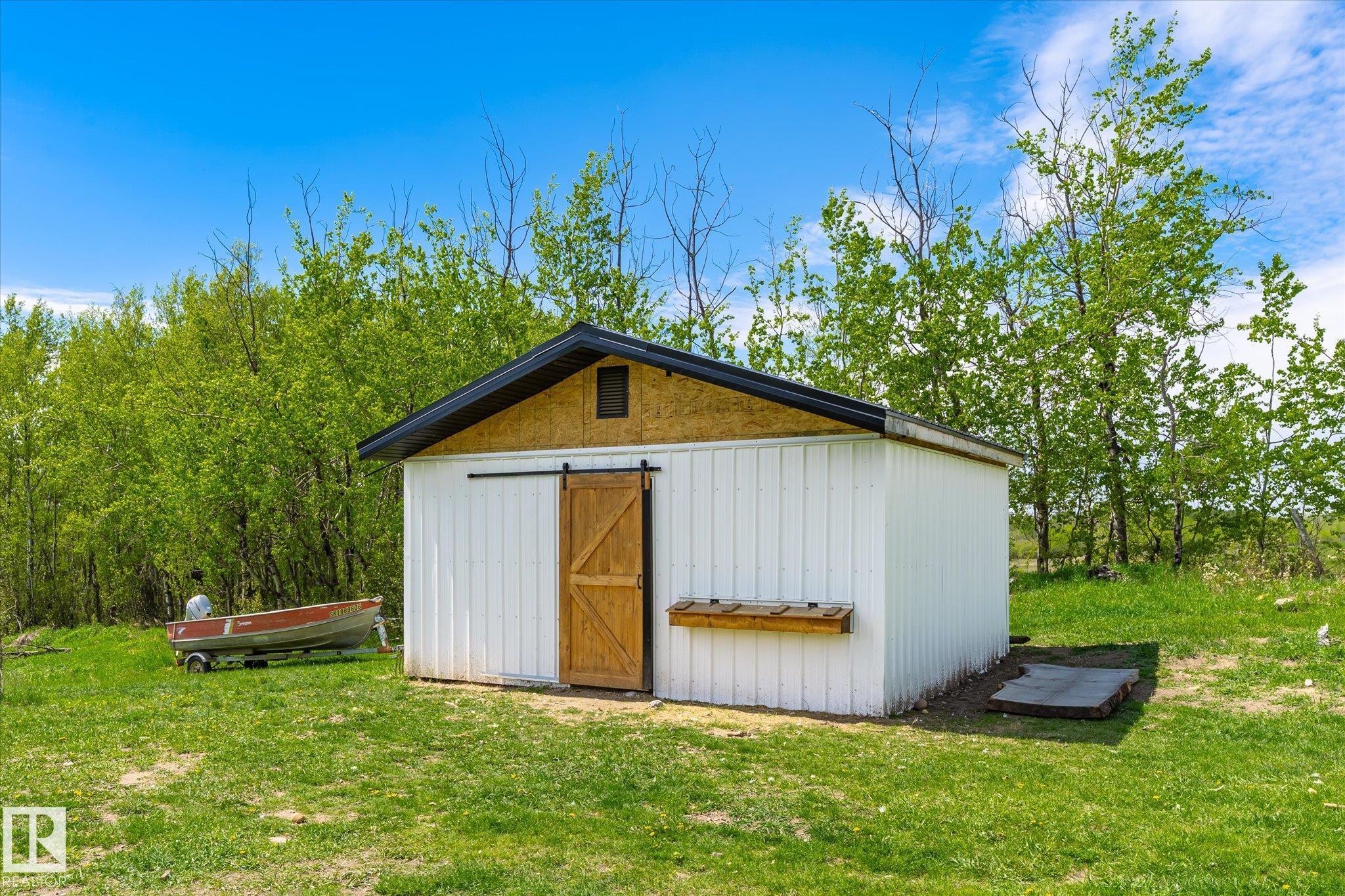 White storage building featuring a dark shingled roof, a natural wood-finish gable, and a wood-finish barn door on a black sliding track - 59102 Rge Road 234, Rural Westlock County, AB