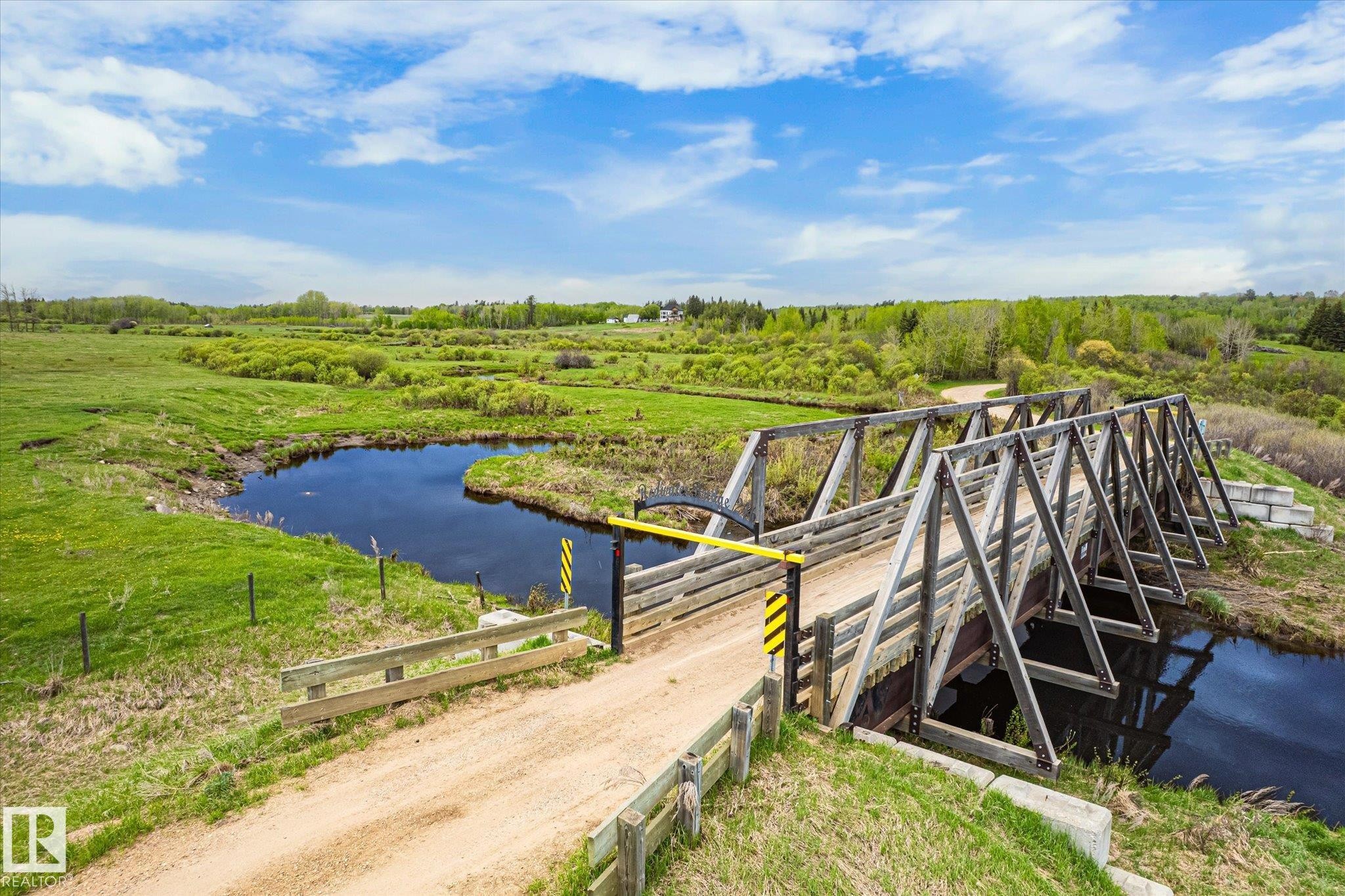 Rural landscape featuring a wooden truss bridge spanning a dark water channel - 59102 Rge Road 234, Rural Westlock County, AB