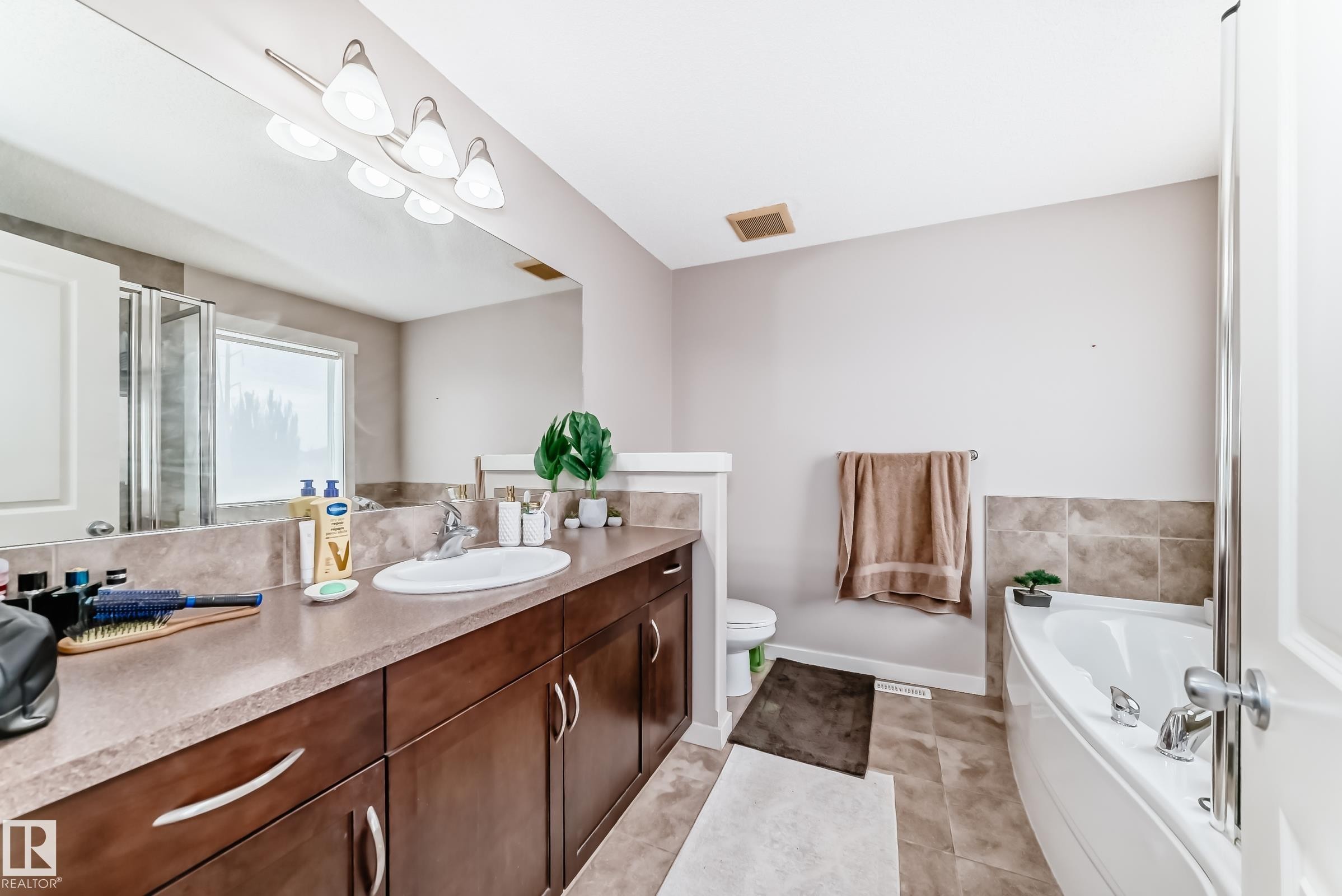 Bathroom with a built-in corner soaking tub, an extended vanity with a single basin sink, and a large wall mirror with overhead lighting - 2808 36 Avenue, Edmonton, AB