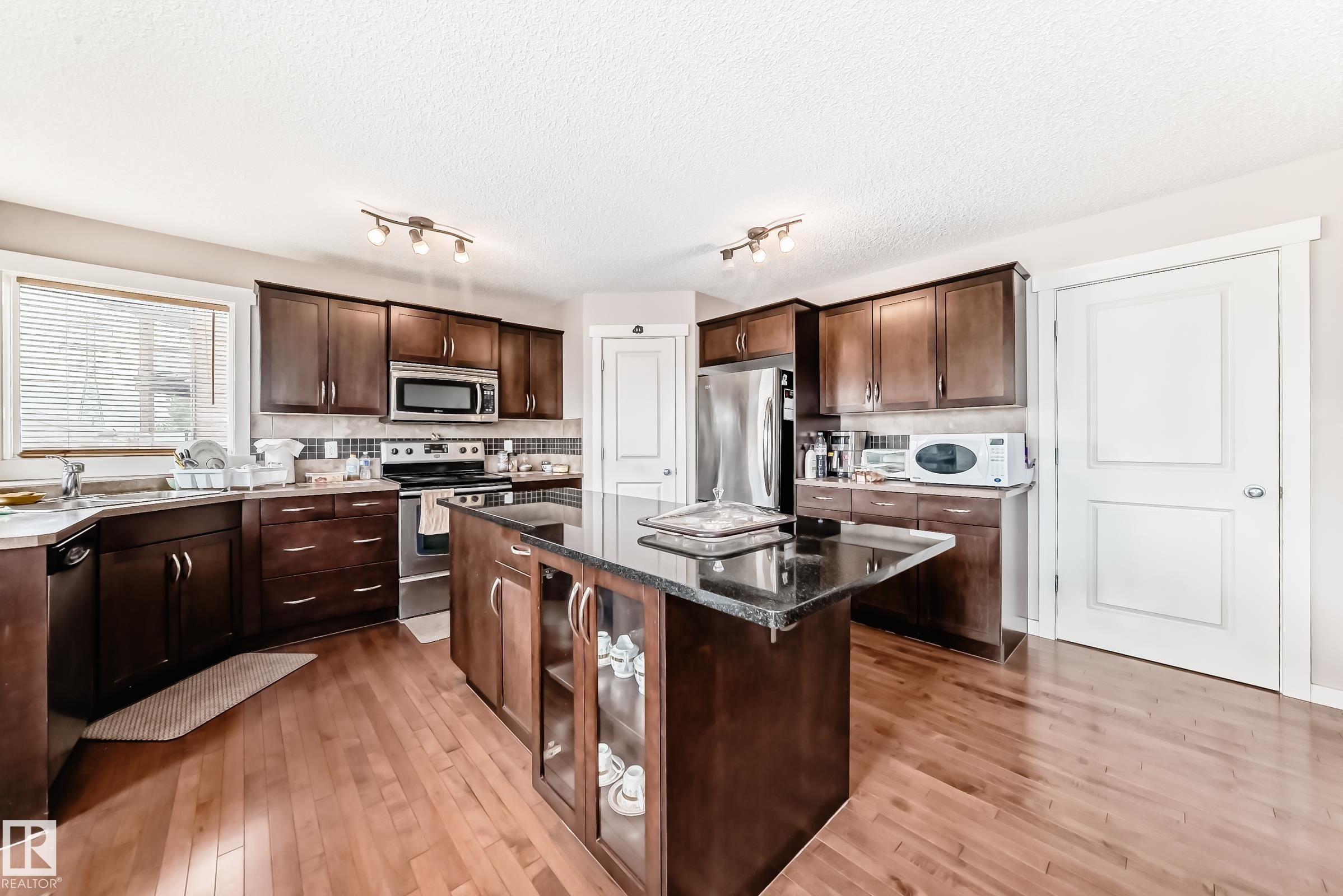 Kitchen featuring dark wood cabinetry, a central island with a dark countertop, wood-finish flooring, and stainless-steel appliances - 2808 36 Avenue, Edmonton, AB