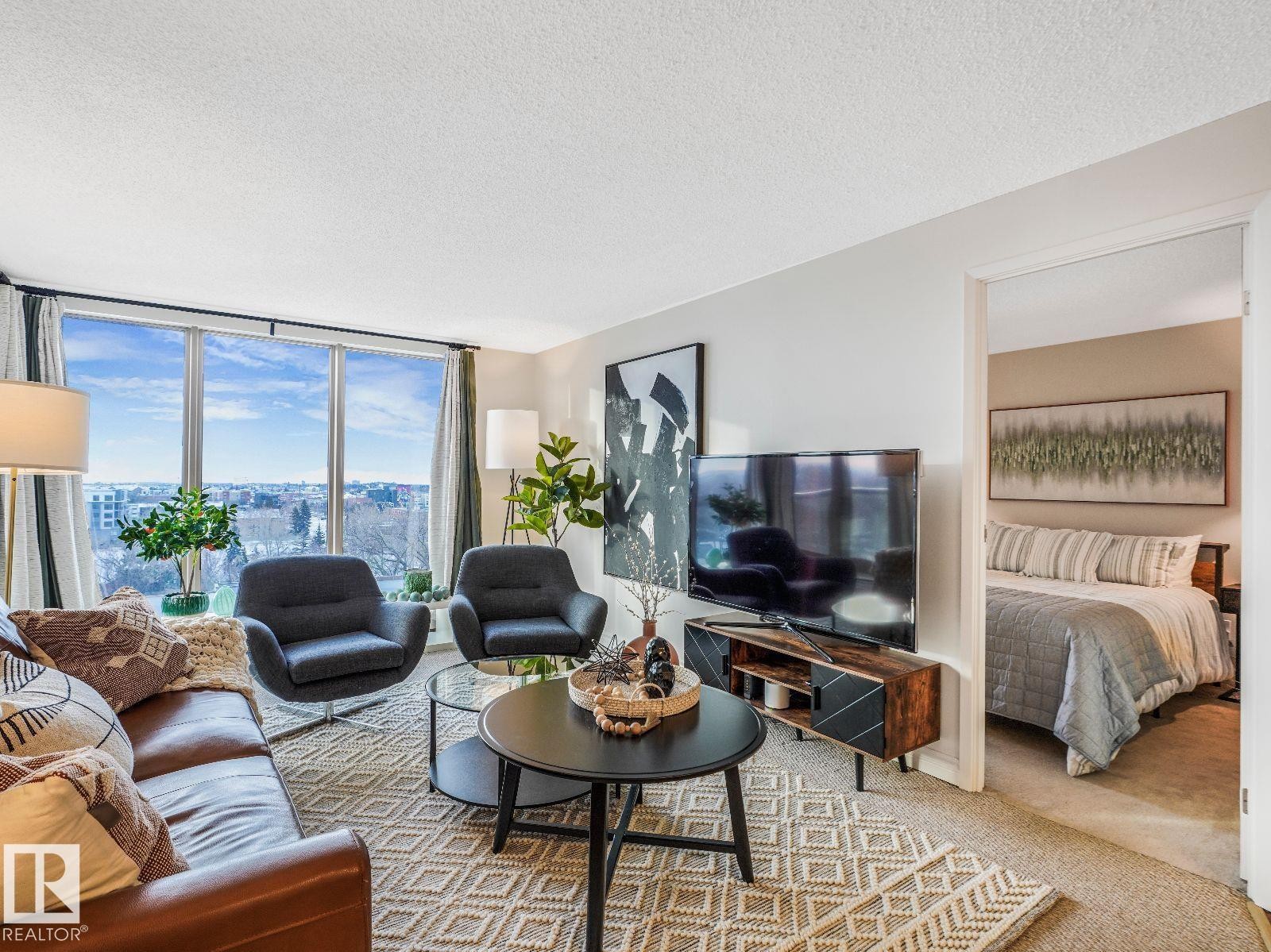 Living area with large picture windows, wood-finish media console, and an open doorway revealing an additional room - 806 10149 Saskatchewan Drive, Edmonton, AB