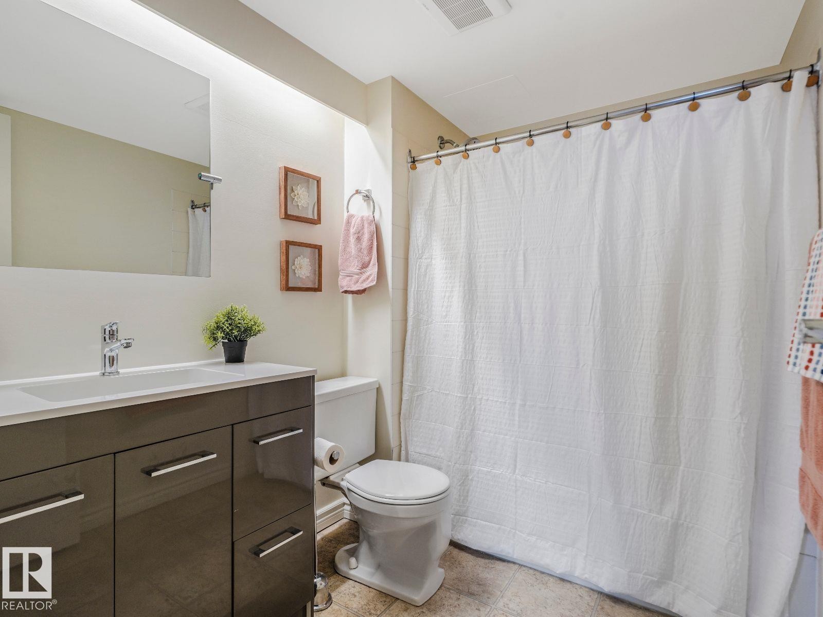 Bathroom featuring a modern vanity with a rectangular sink, chrome faucet, wall-mounted mirror, and a full bathtub with a shower rod - 806 10149 Saskatchewan Drive, Edmonton, AB