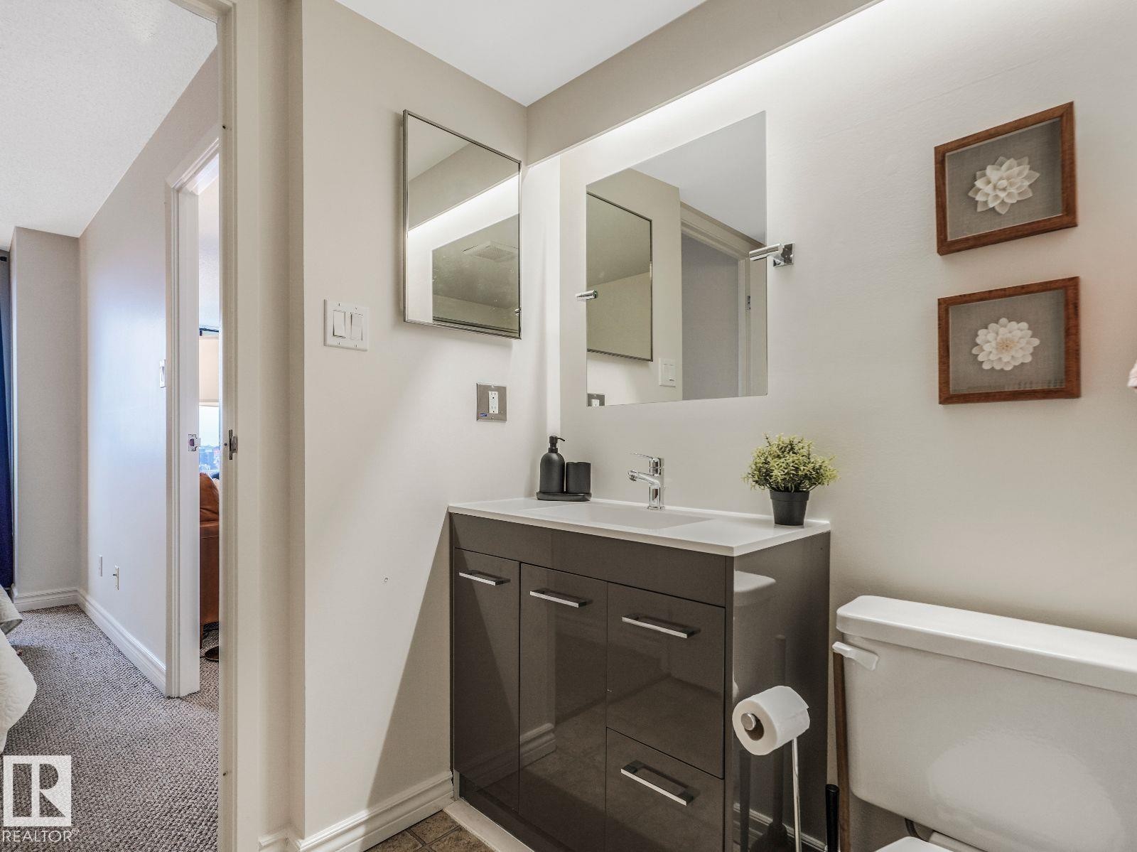 Bathroom featuring a modern vanity with integrated sink, chrome faucet, and mirrored medicine cabinet - 806 10149 Saskatchewan Drive, Edmonton, AB