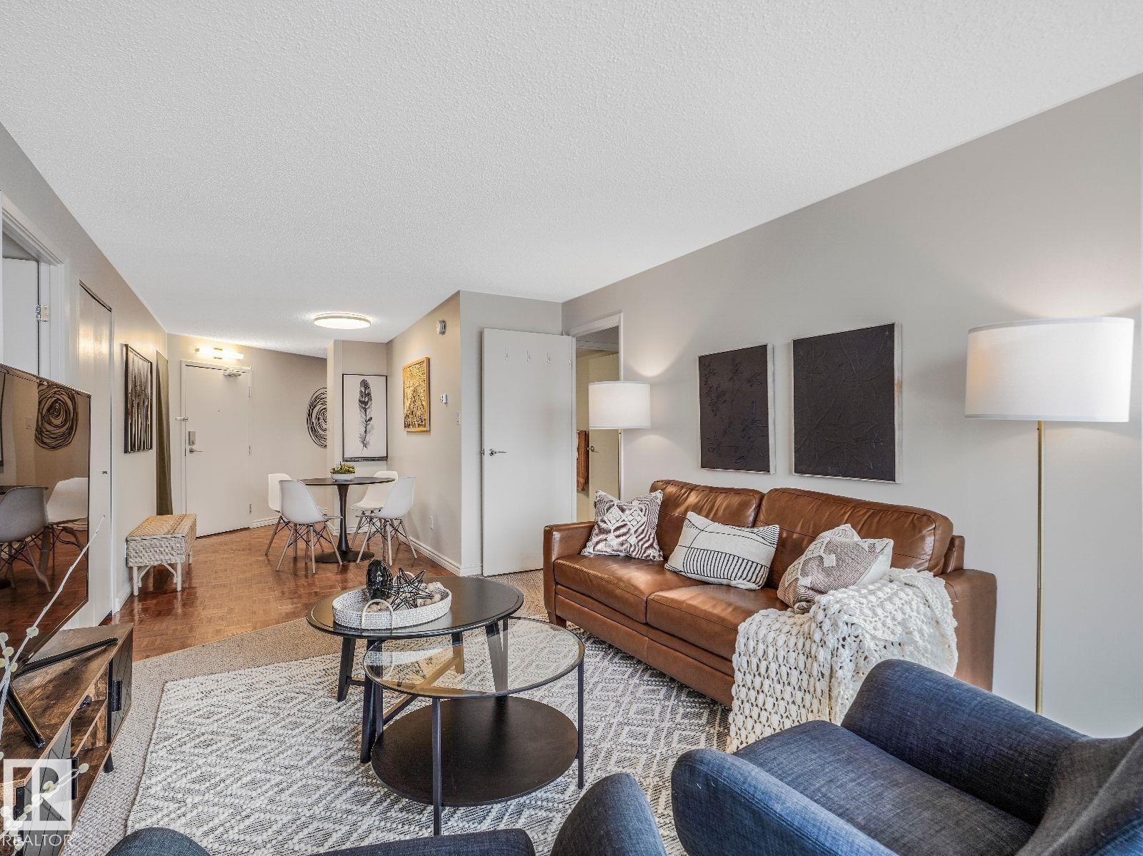 Open concept living area featuring wood-finish flooring, light grey wall paint, and a textured area rug - 806 10149 Saskatchewan Drive, Edmonton, AB