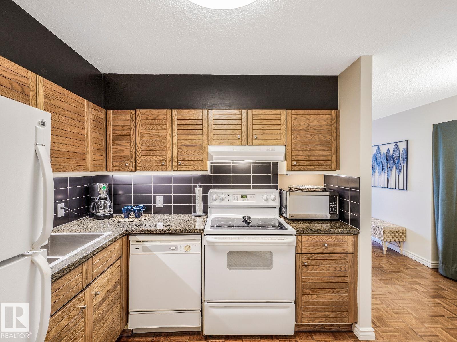 Kitchen featuring wood-finish cabinetry, dark tile backsplash, and speckled countertops - 806 10149 Saskatchewan Drive, Edmonton, AB