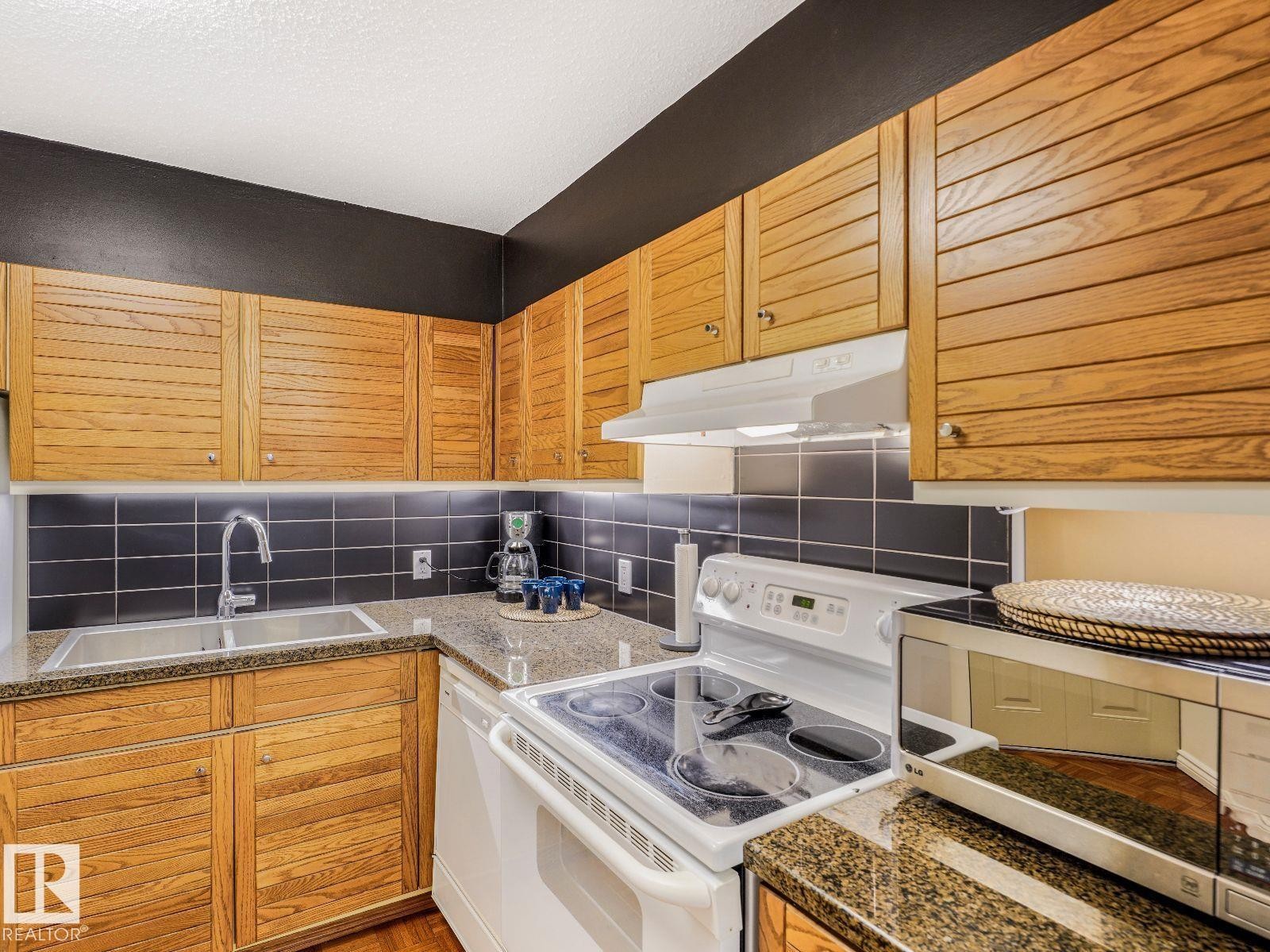 Kitchen featuring wood-finish cabinetry, dark subway tile backsplash, and stone countertops - 806 10149 Saskatchewan Drive, Edmonton, AB