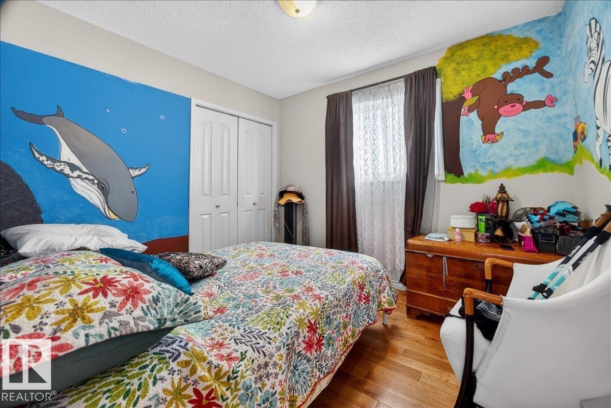 Bedroom featuring wood-finish flooring, a double-door closet, and a ceiling-mounted light fixture - 5108 138A Avenue, Edmonton, AB