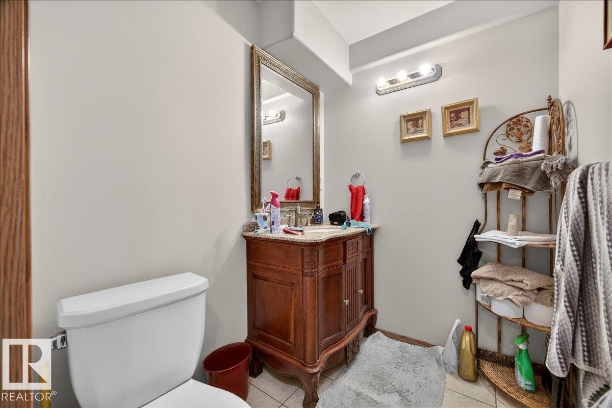 Bathroom featuring a vanity with a carved wood-finish base, a decorative framed mirror, and a white toilet - 5108 138A Avenue, Edmonton, AB