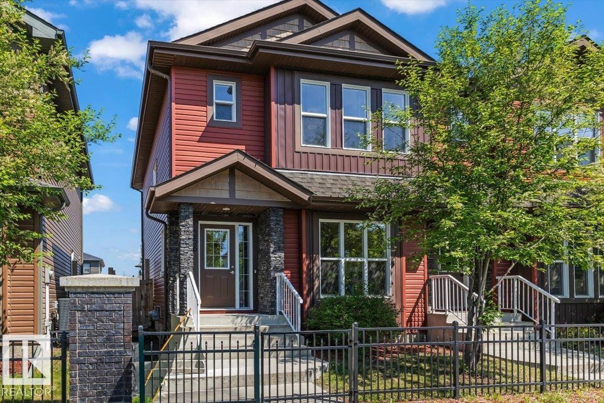 Two-story residence featuring a covered front entry with stone-clad columns, red siding, and multiple windows - 356 Pioneer Road, Spruce Grove, AB