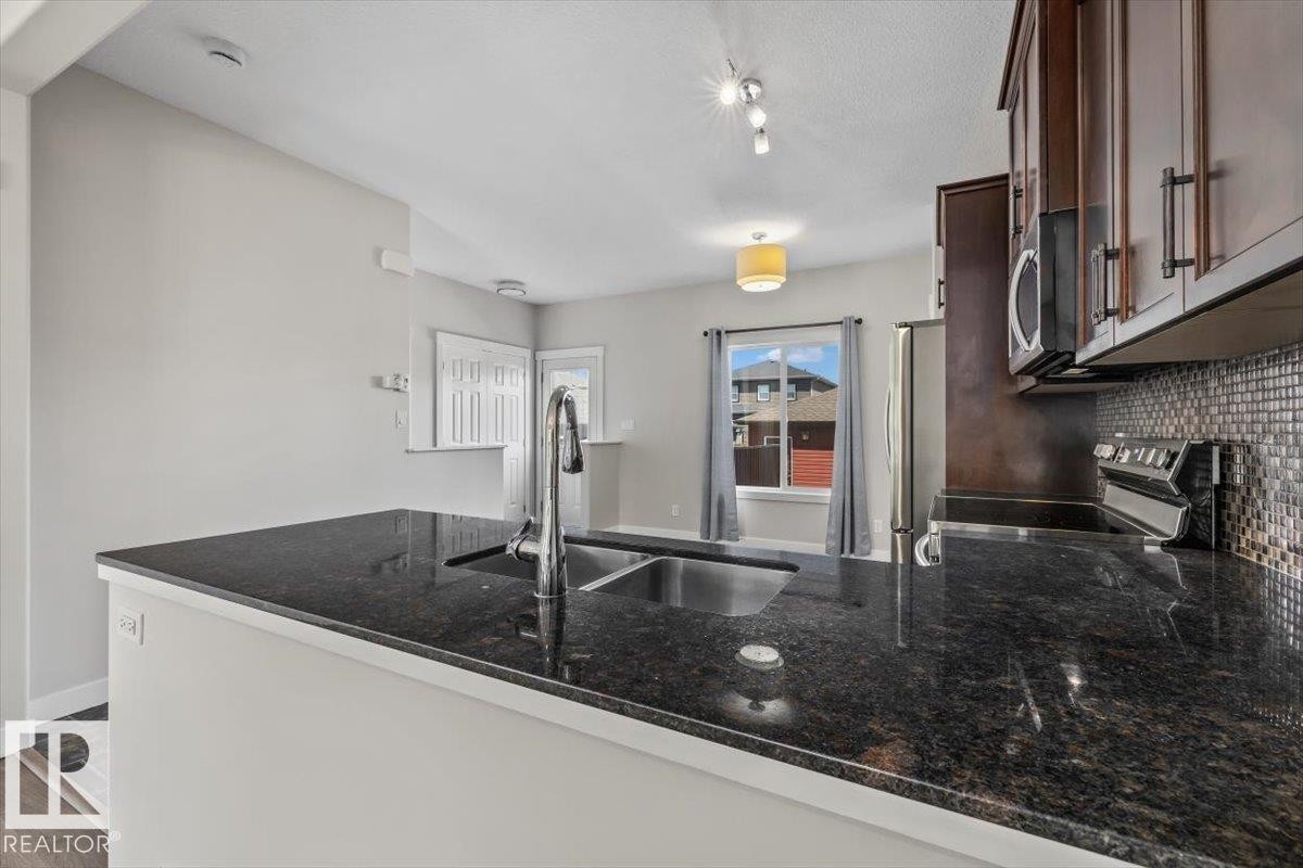 Kitchen featuring a double basin sink with a high-arc faucet, dark granite countertops, and mosaic tile backsplash - 356 Pioneer Road, Spruce Grove, AB