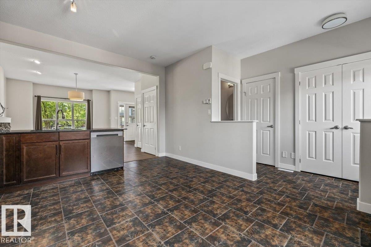 Spacious open-concept area featuring durable tile flooring, rich wood-finish cabinetry, a stainless steel dishwasher, and multiple paneled doors - 356 Pioneer Road, Spruce Grove, AB