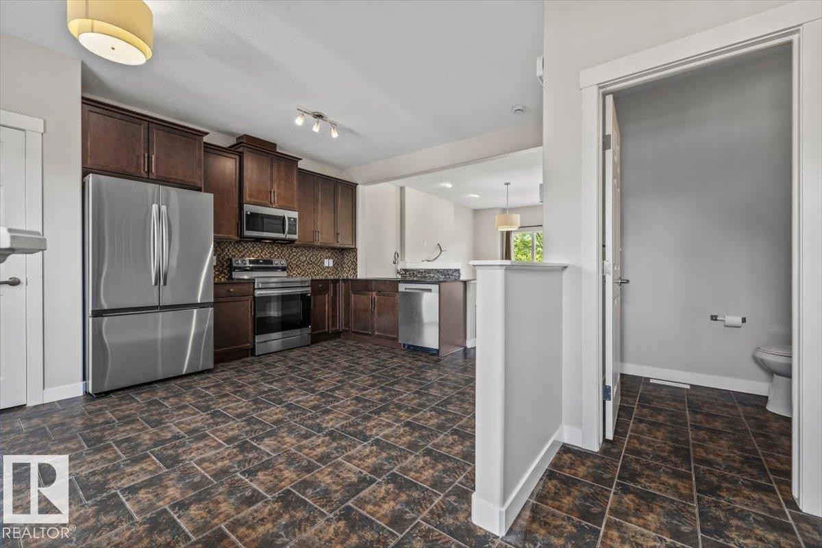 Kitchen featuring dark wood cabinetry, stainless steel appliances, and a mosaic tile backsplash - 356 Pioneer Road, Spruce Grove, AB