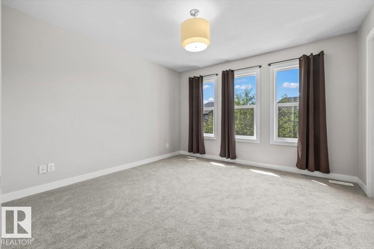 Carpeted room with light gray walls, featuring three windows with dark curtains, white trim, and a ceiling-mounted drum light fixture - 356 Pioneer Road, Spruce Grove, AB