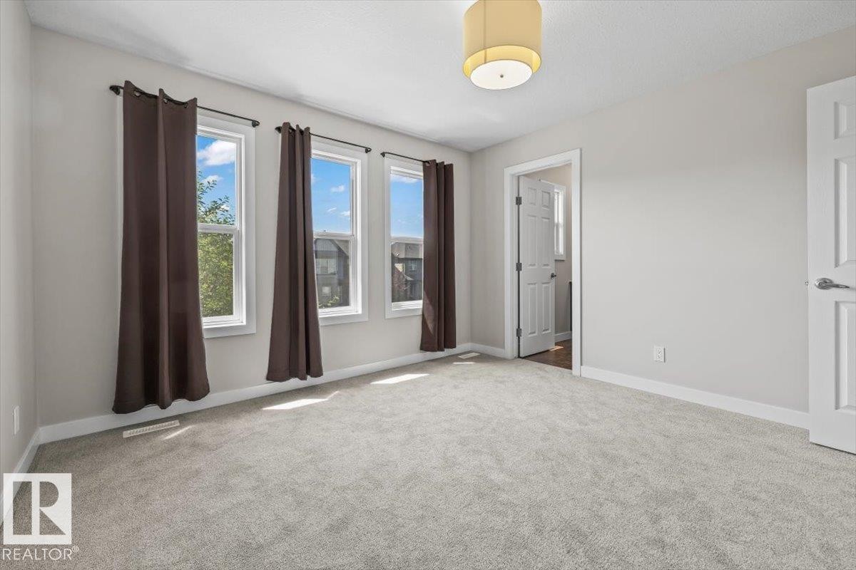 Spacious room featuring light gray carpet flooring, three large windows, a neutral wall color, white trim, and a modern drum light fixture - 356 Pioneer Road, Spruce Grove, AB