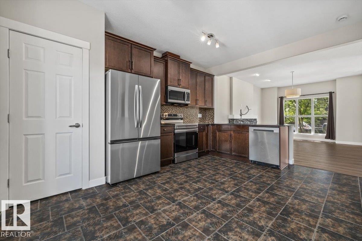 Kitchen featuring dark wood cabinetry, stainless steel appliances, and a tiled backsplash - 356 Pioneer Road, Spruce Grove, AB