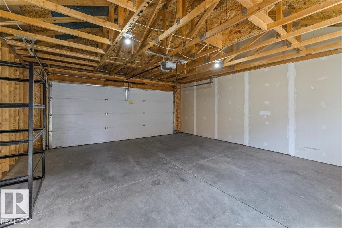 Spacious garage featuring a concrete floor, exposed wood ceiling trusses, and drywall-ready walls - 356 Pioneer Road, Spruce Grove, AB