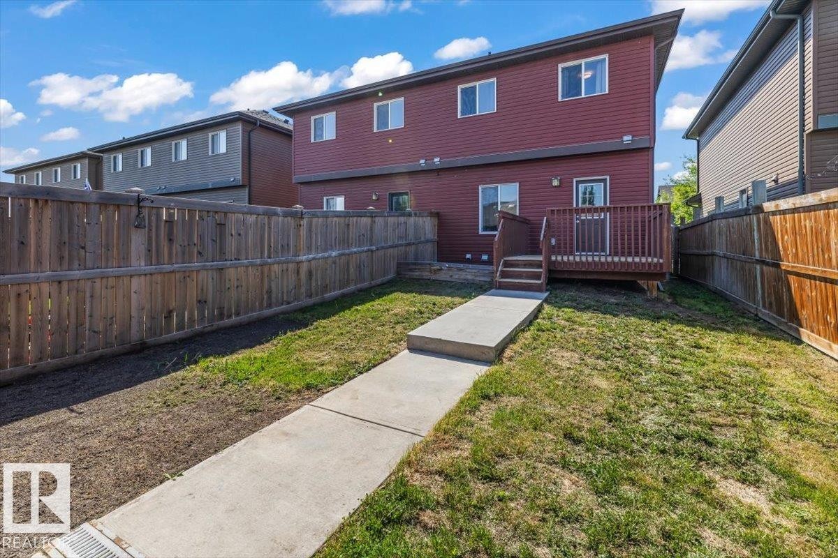 Rear exterior featuring a wood deck with stairs, a concrete pathway, and a fully fenced yard with wood panel fencing - 356 Pioneer Road, Spruce Grove, AB