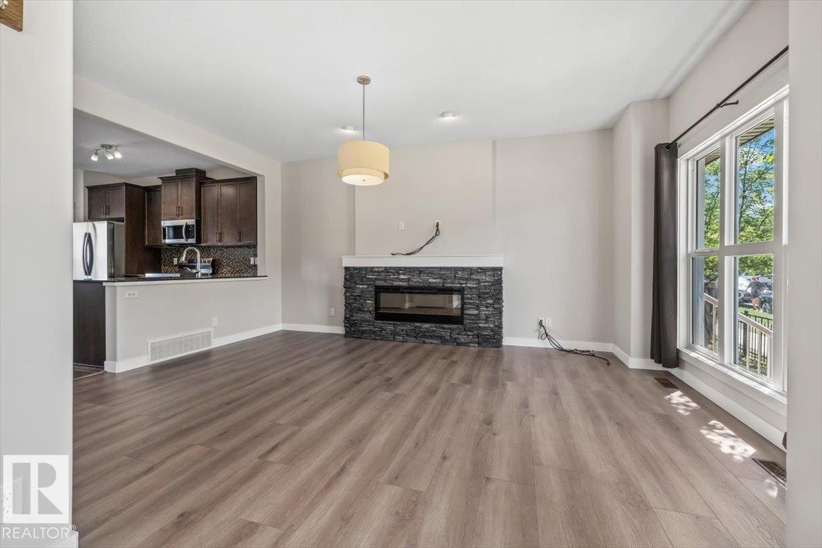 Spacious living area featuring wood-finish flooring, a stone-clad fireplace with an electric insert, and a large multi-pane window - 356 Pioneer Road, Spruce Grove, AB