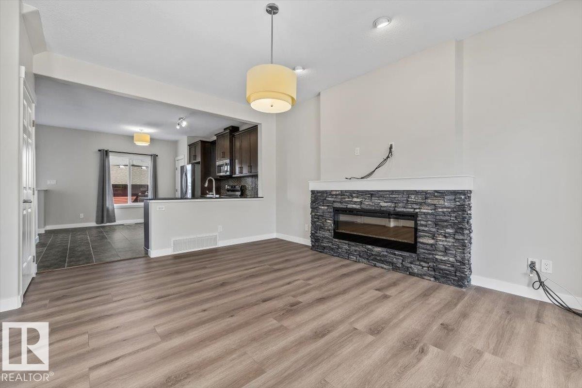Living area featuring wood-finish flooring, a contemporary fireplace with a stacked stone facade, and a drum pendant light fixture - 356 Pioneer Road, Spruce Grove, AB