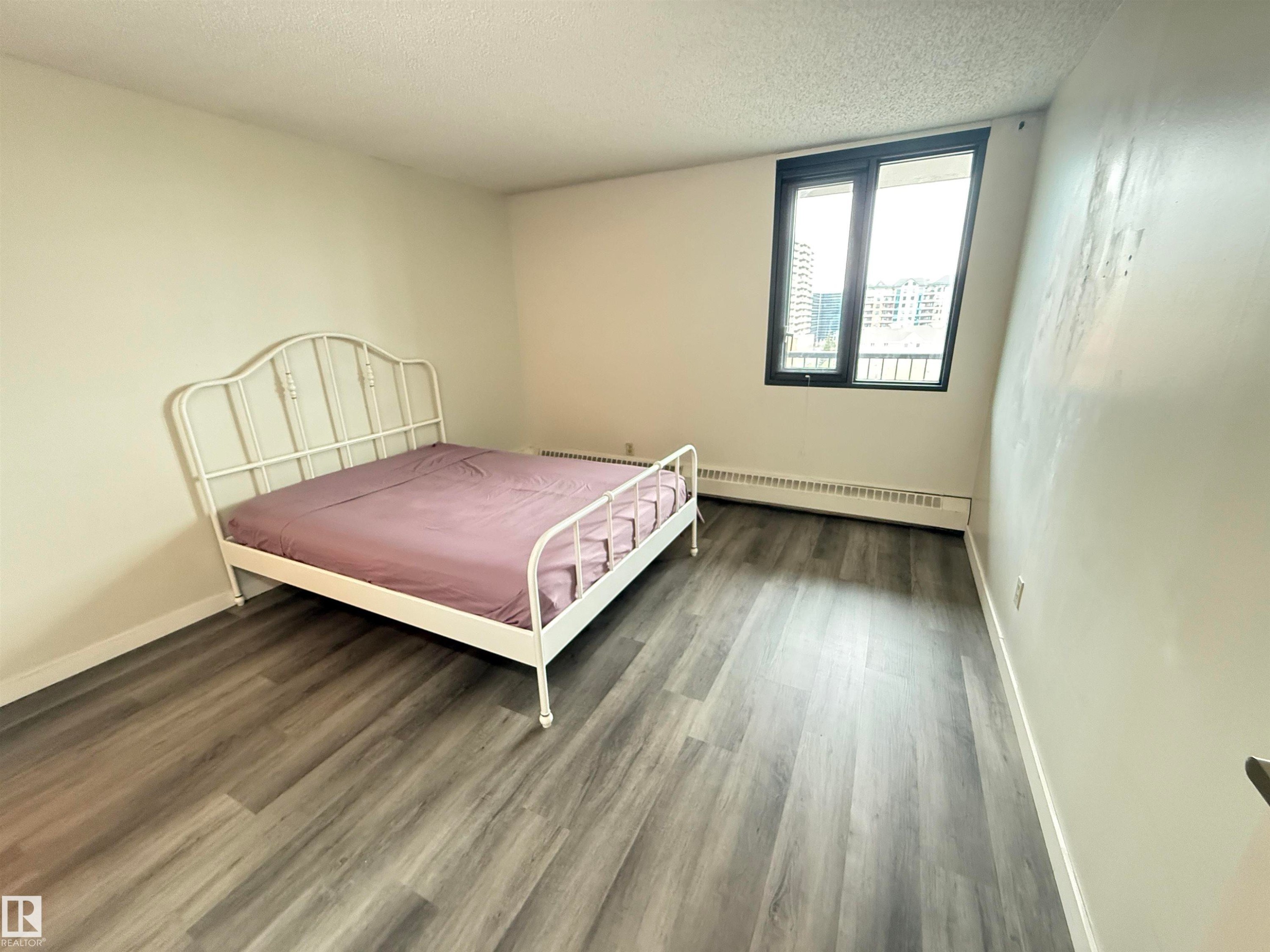 Room featuring neutral painted walls, wood-finish flooring, and a large window with black framing - #706 10125 109 St Nw, Edmonton, AB