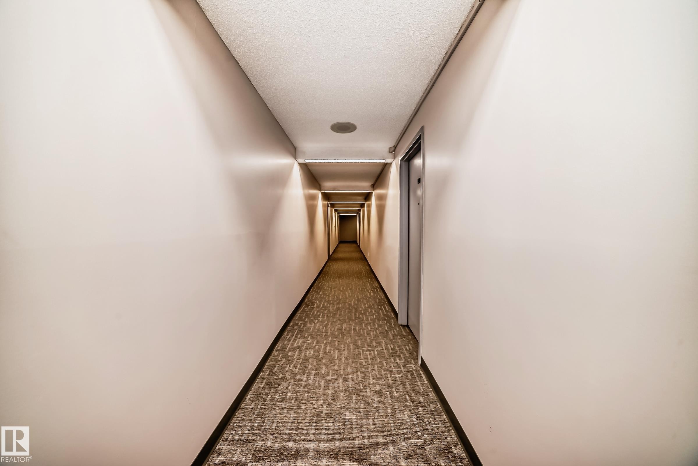 Long hallway featuring neutral-toned walls, recessed ceiling lighting, a textured carpet runner, and multiple entry doors - #706 10125 109 St Nw, Edmonton, AB