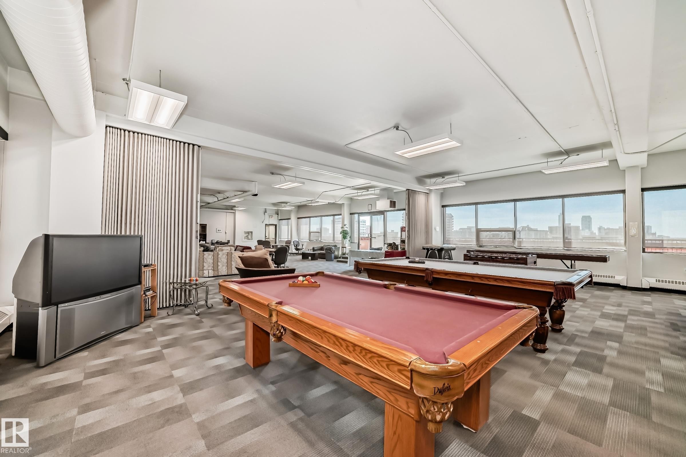Expansive entertainment area featuring two pool tables, patterned carpet flooring, and abundant natural light from numerous windows - #706 10125 109 St Nw, Edmonton, AB