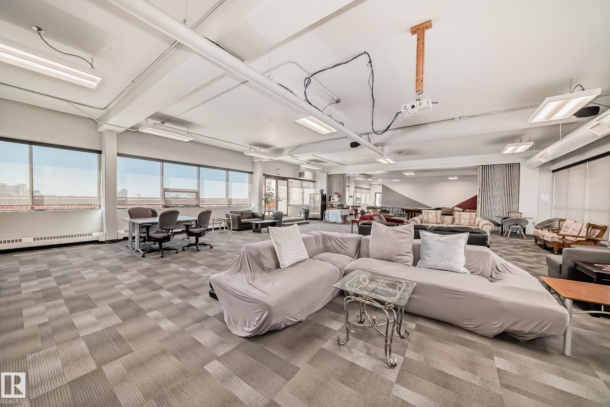 Expansive open-concept room featuring wide windows, patterned carpet flooring, and exposed ceiling ductwork - #706 10125 109 St Nw, Edmonton, AB