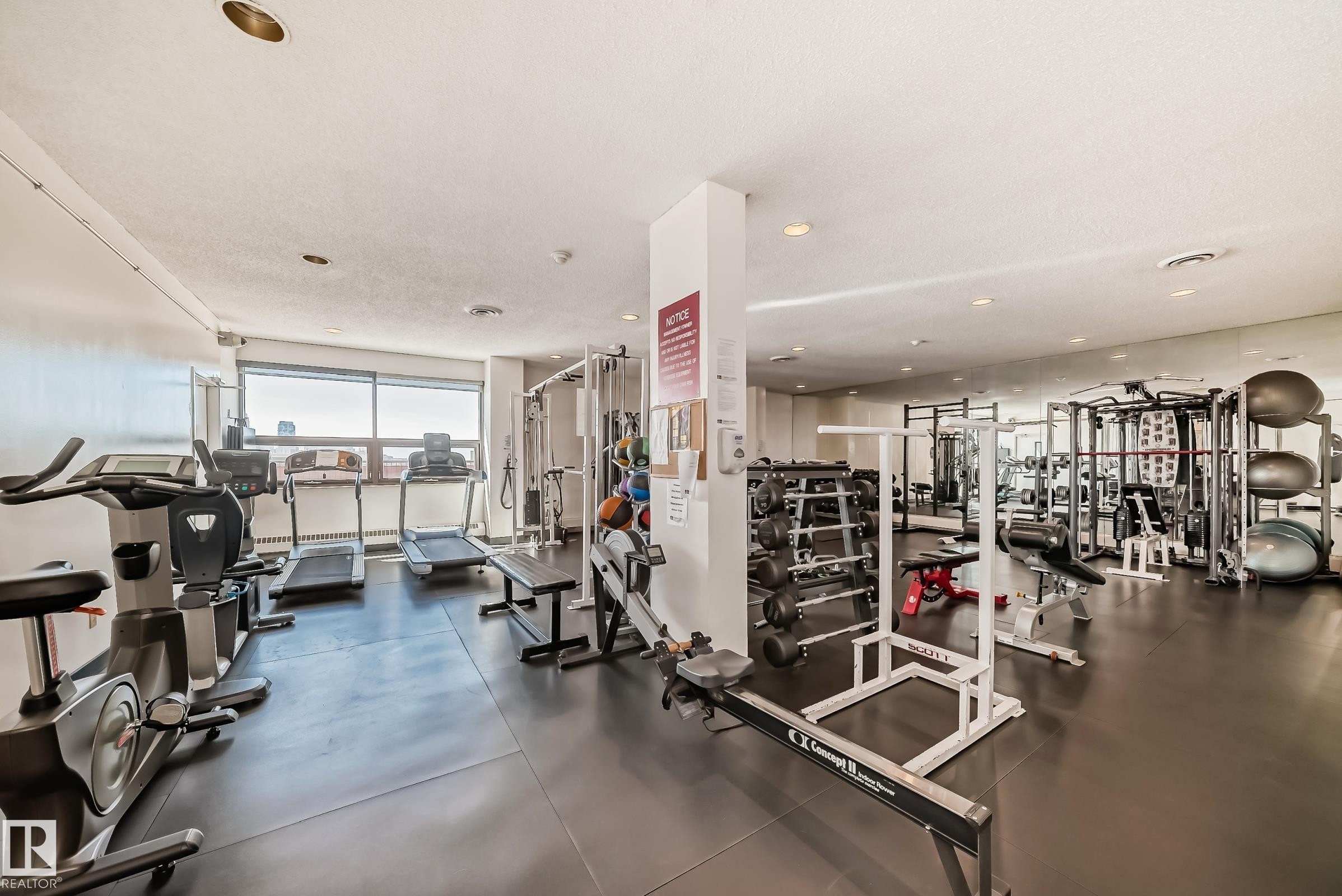 Dedicated fitness center featuring ample cardio equipment, weight training machines, a free weight area, reflective wall panels, and large perimeter windows - #706 10125 109 St Nw, Edmonton, AB