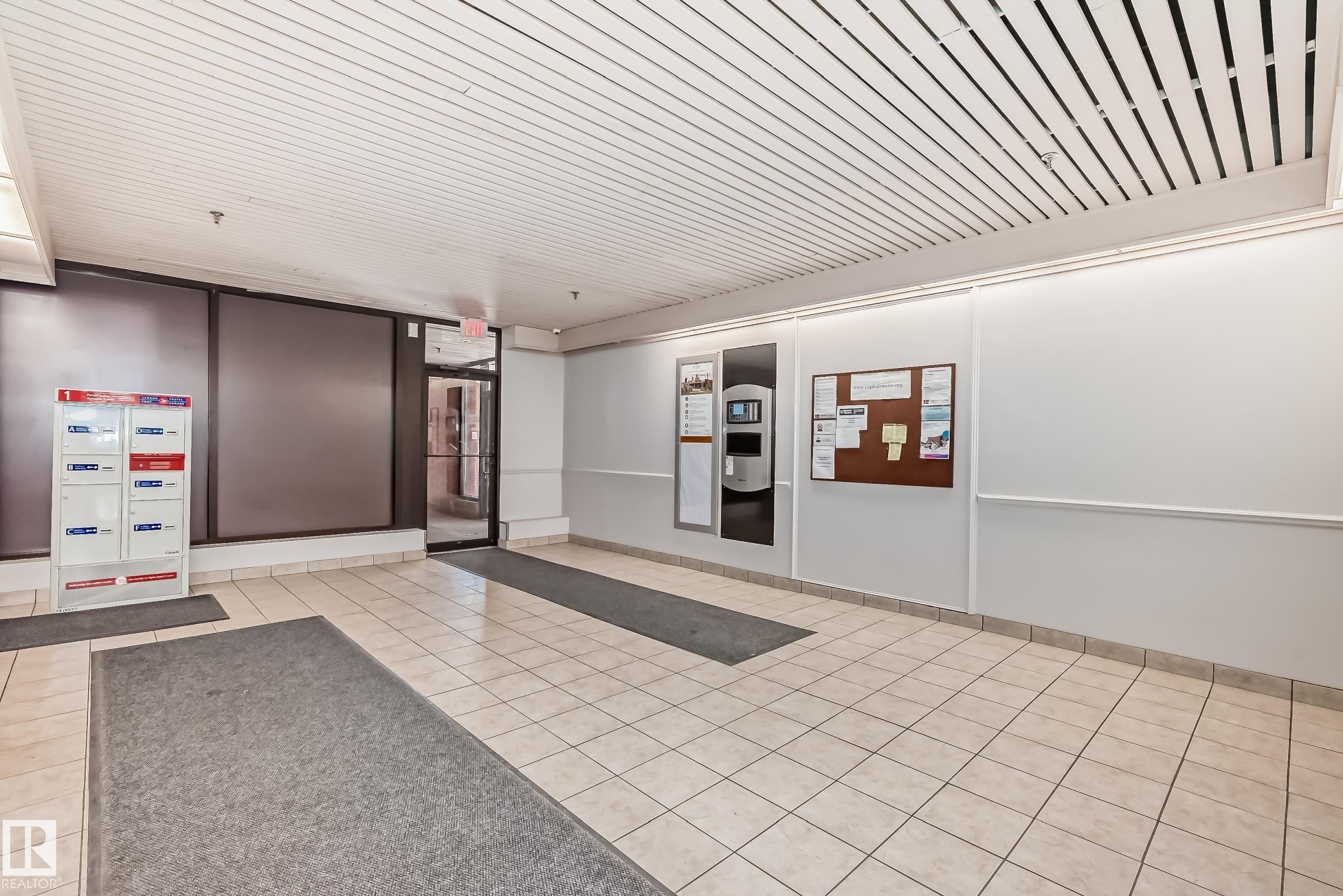 Building entryway featuring light-toned square floor tiles, a grid-patterned ceiling, and an illuminated information board - #706 10125 109 St Nw, Edmonton, AB