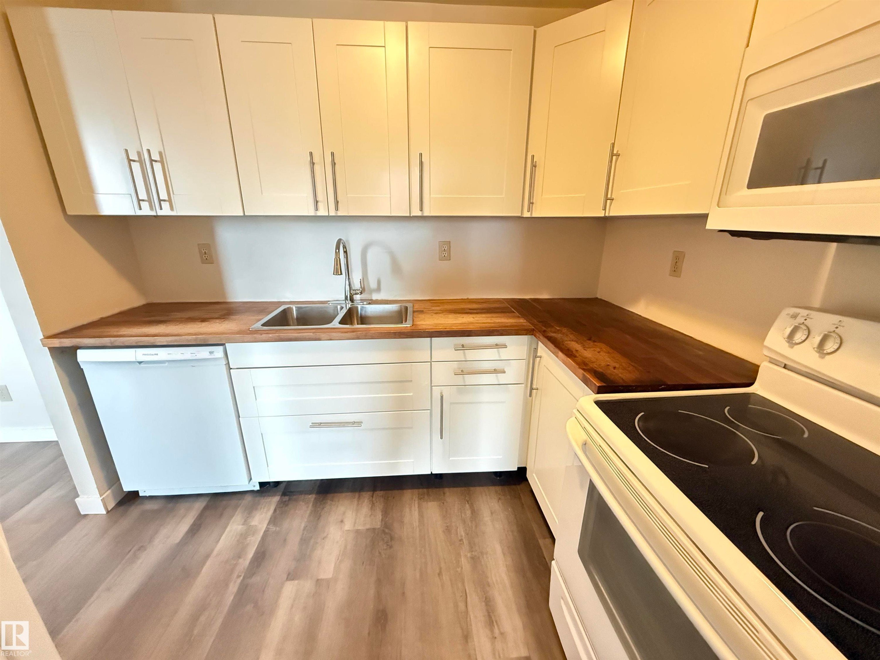 Kitchen featuring white shaker-style cabinetry, wood-finish countertops, stainless steel double basin sink with a high-arc faucet, and wood-finish flooring - #706 10125 109 St Nw, Edmonton, AB
