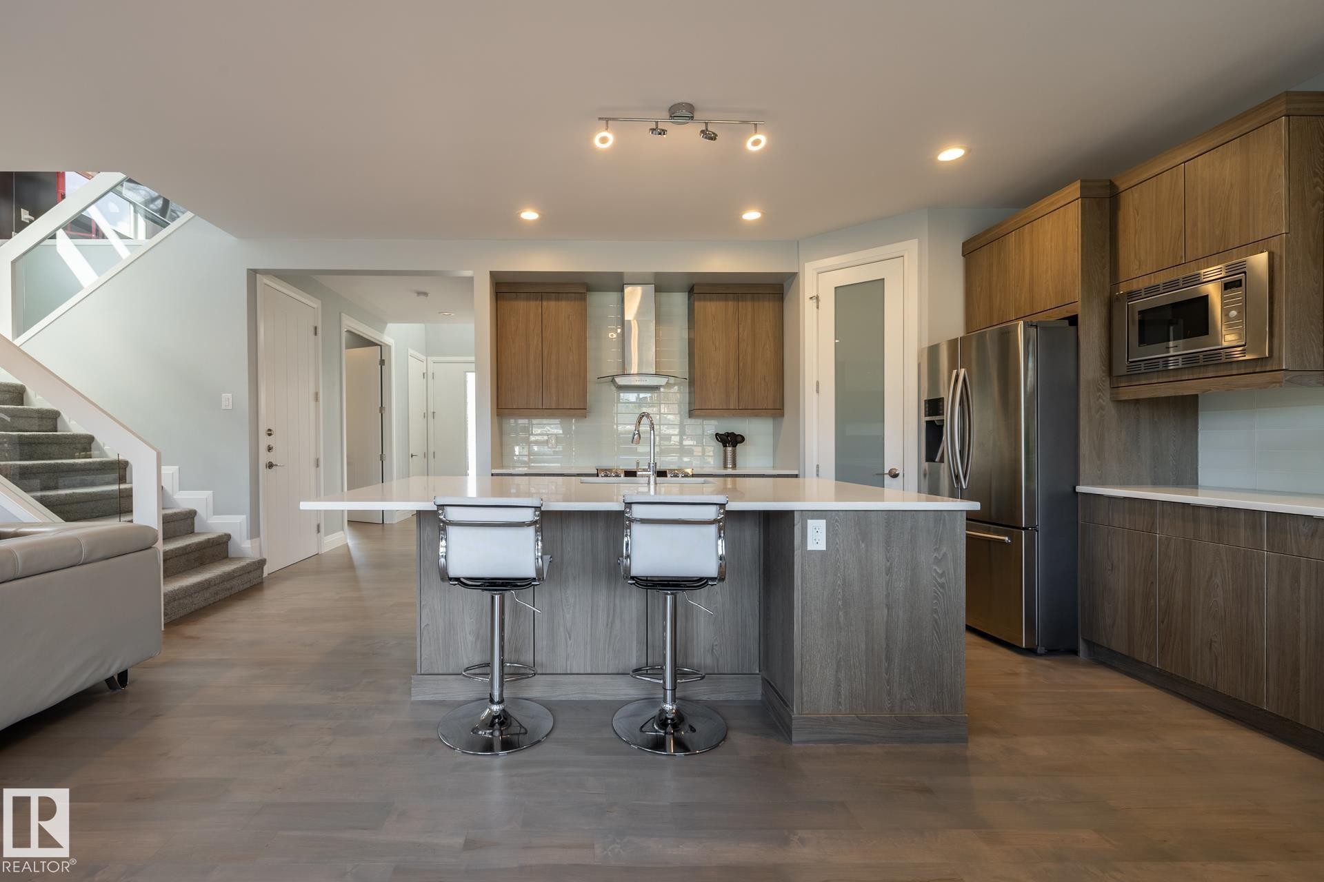 Kitchen featuring modern cabinets, decorative backsplash, a kitchen breakfast bar, appliances with stainless steel finishes, and a kitchen island with sink - 10936 71 Avenue, Edmonton, AB