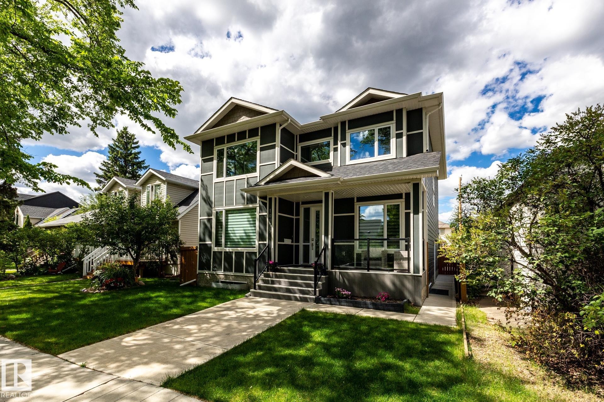 Contemporary two-story residence featuring dark siding with white trim accents, a prominent covered front porch with black railings, and a concrete walkway leading to the entrance - 10936 71 Avenue, Edmonton, AB
