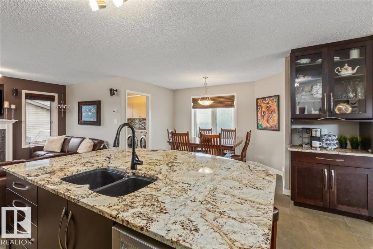 Kitchen island featuring a dual basin sink with a matte black high-arc faucet, granite countertops, and dark wood cabinetry - 1086 Grantham Drive Nw, Edmonton, AB - Indoor Photo Showing Kitchen With Double Sink