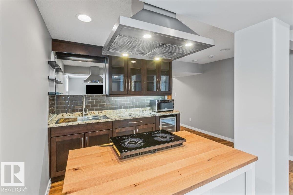 Modern kitchen with an induction cooktop island, granite countertops, dark wood-finish cabinetry, subway tile backsplash, and a stainless steel range hood - 1086 Grantham Drive Nw, Edmonton, AB - Indoor Photo Showing Other Room